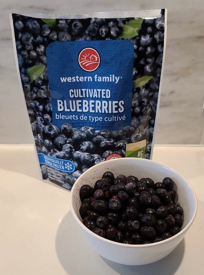 Blueberries in a white bowl in front of a bag of frozen blueberries on a counter