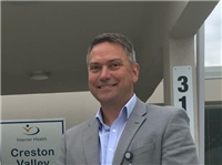 Man in blue shirt, grey suit jacket, with grey hair smiles. 