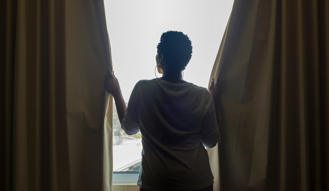 Person facing window, closing dark window curtains.