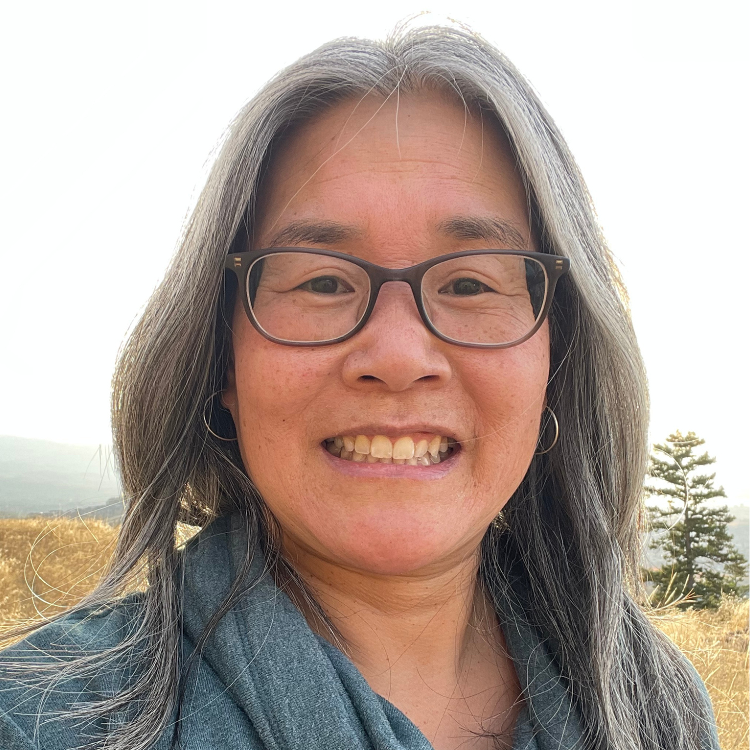 a person with long grey hair and glasses looks to camera