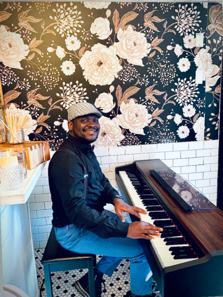 Person playing a piano in a room with floral wallpaper.
