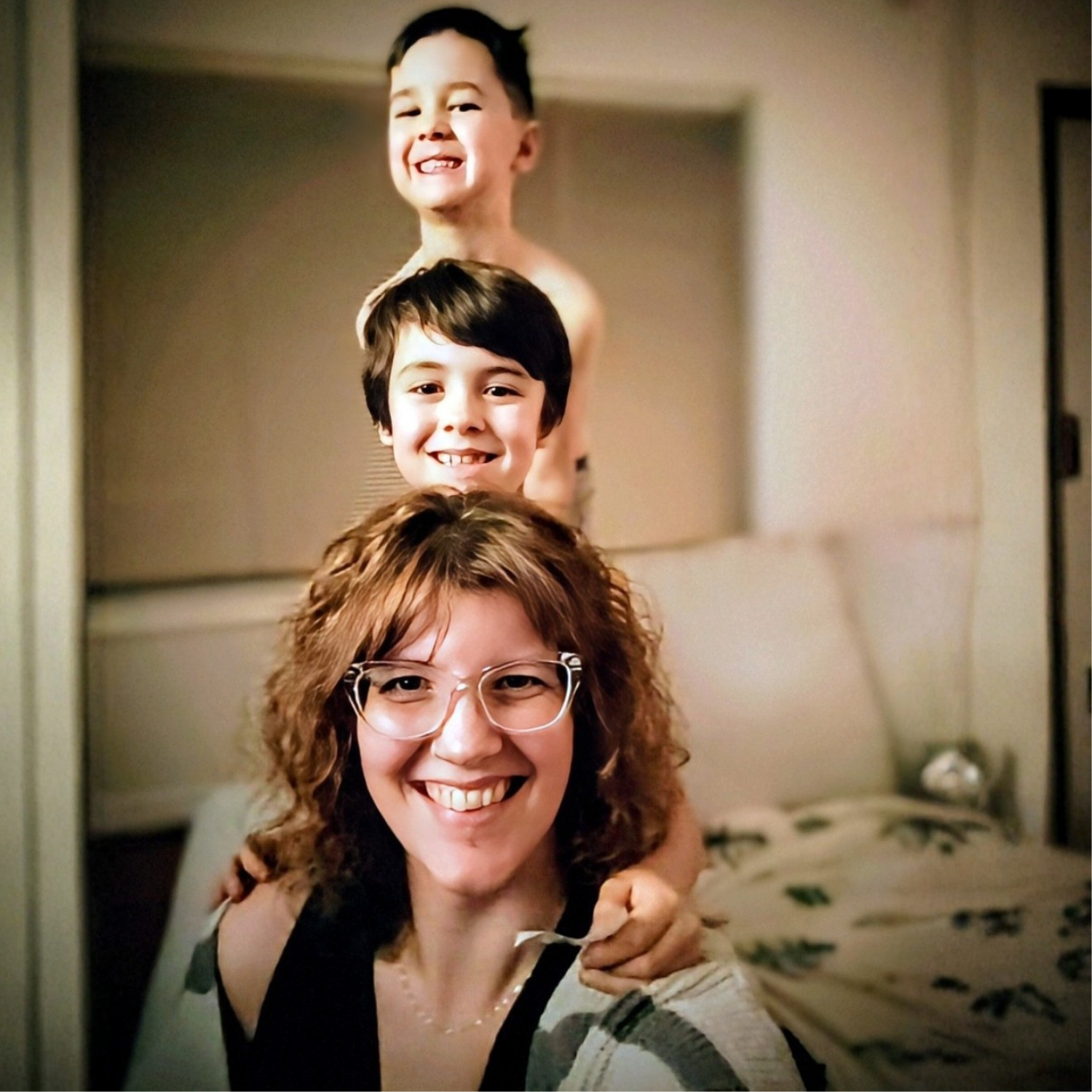 One dark-haired adult and two dark-haired children standing in a vertical line smiling at the camera.