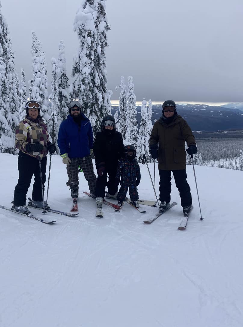 A group of three adults and two children on skis posing at the top of a mountain