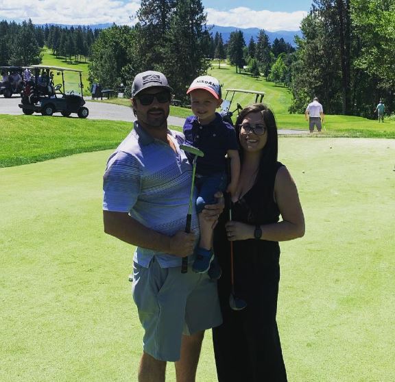 A man in golf attire holds a putter and a young child next to a woman in black clothing