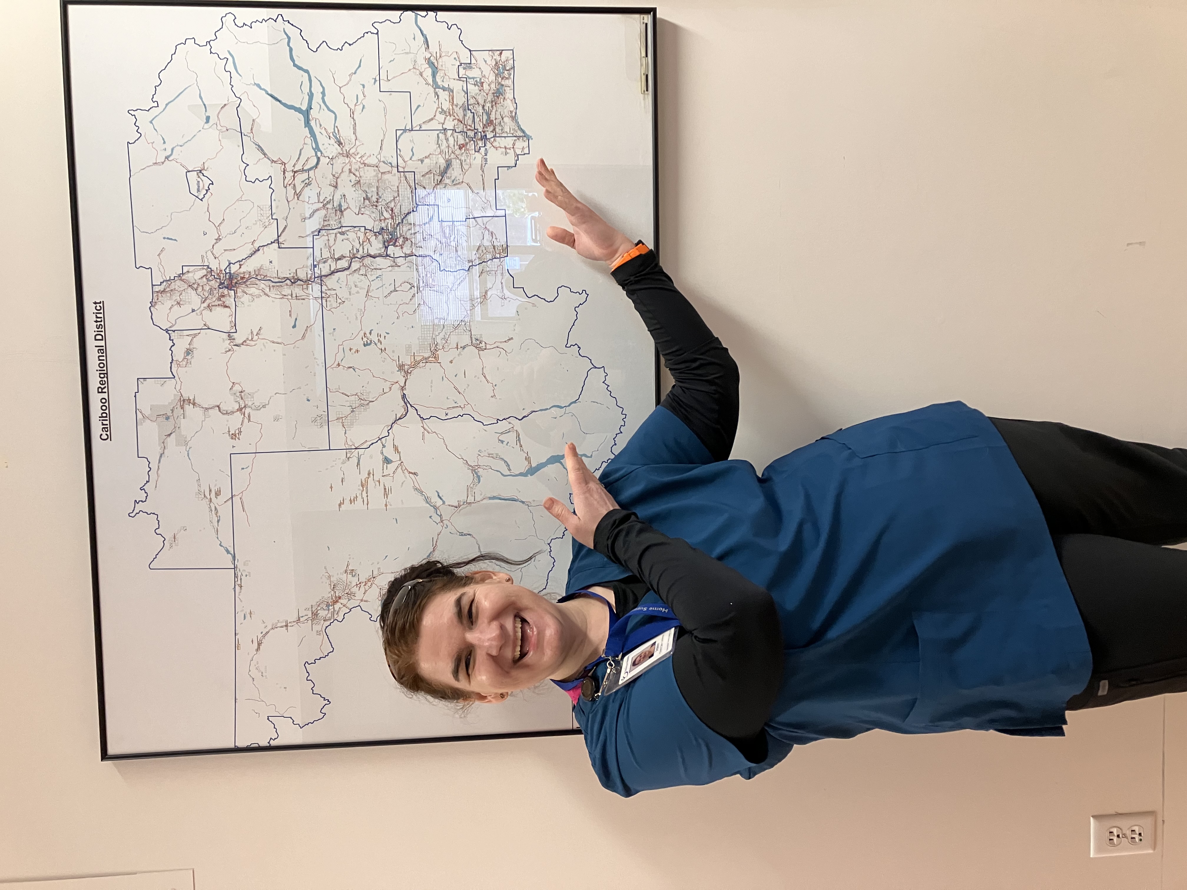 A laughing woman in blue medical clothes points at a map on a wall