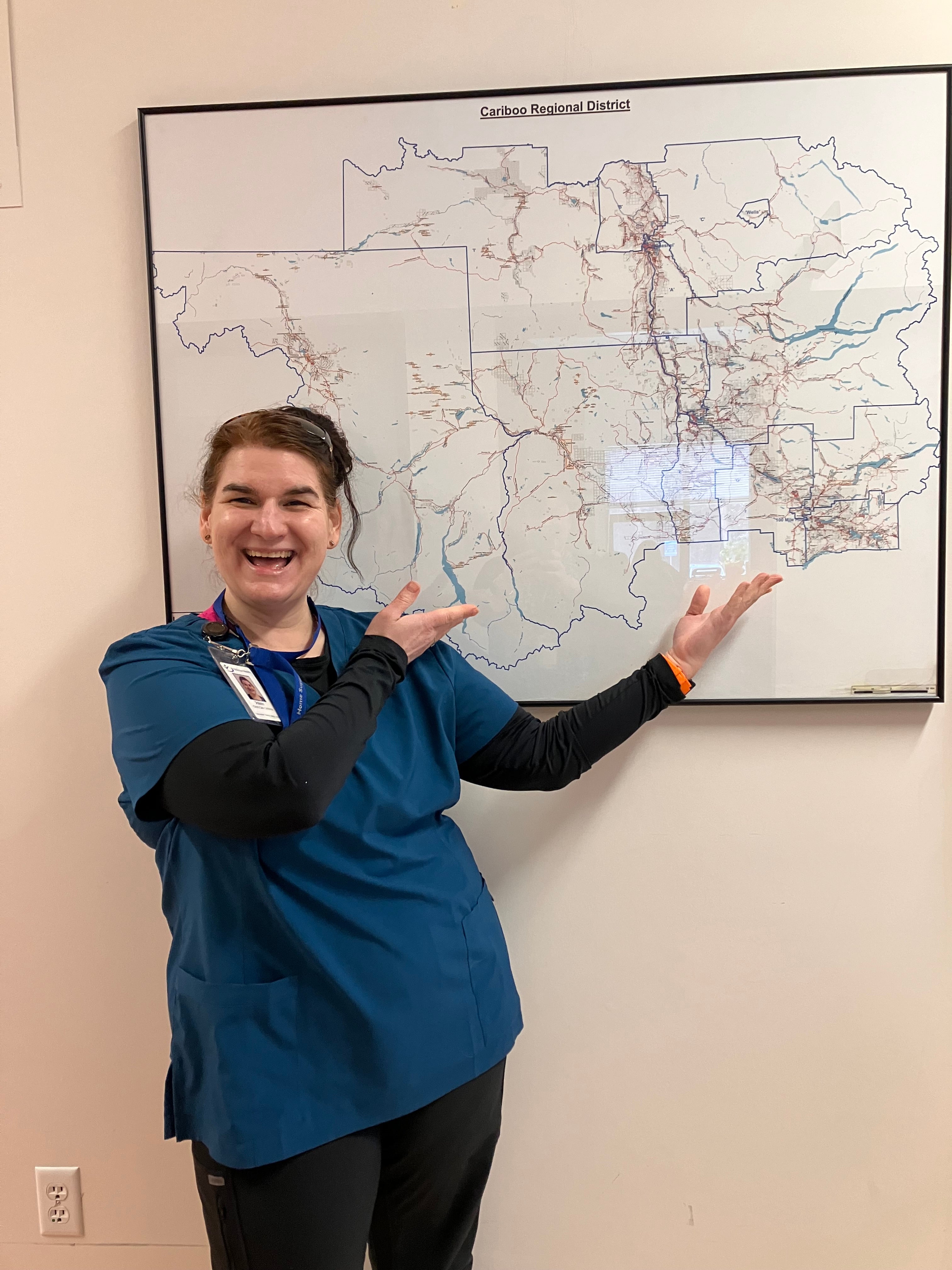 A laughing woman in blue medical clothes points at a map on a wall