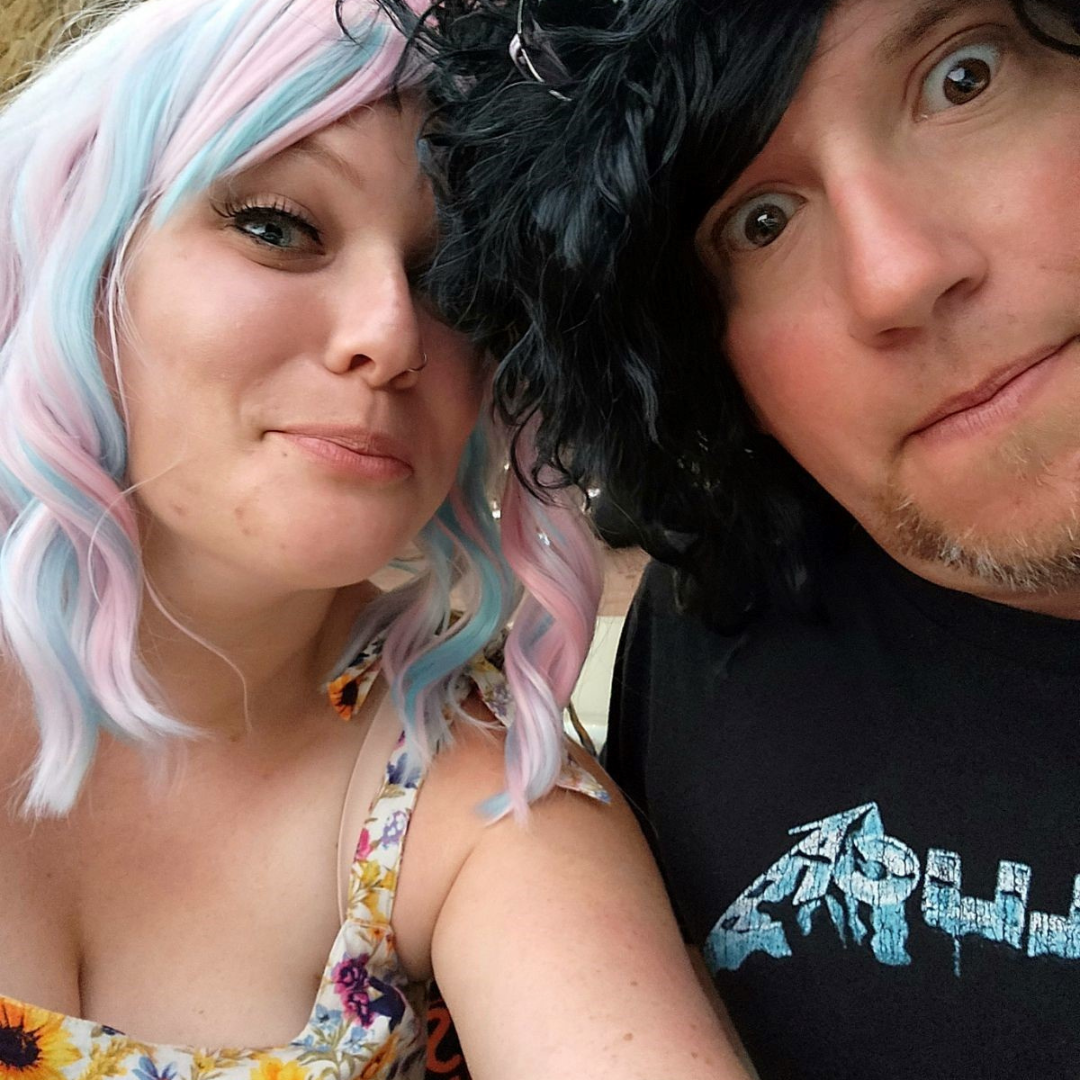 A woman wearing a colourful wig poses with a man wearing a black wig