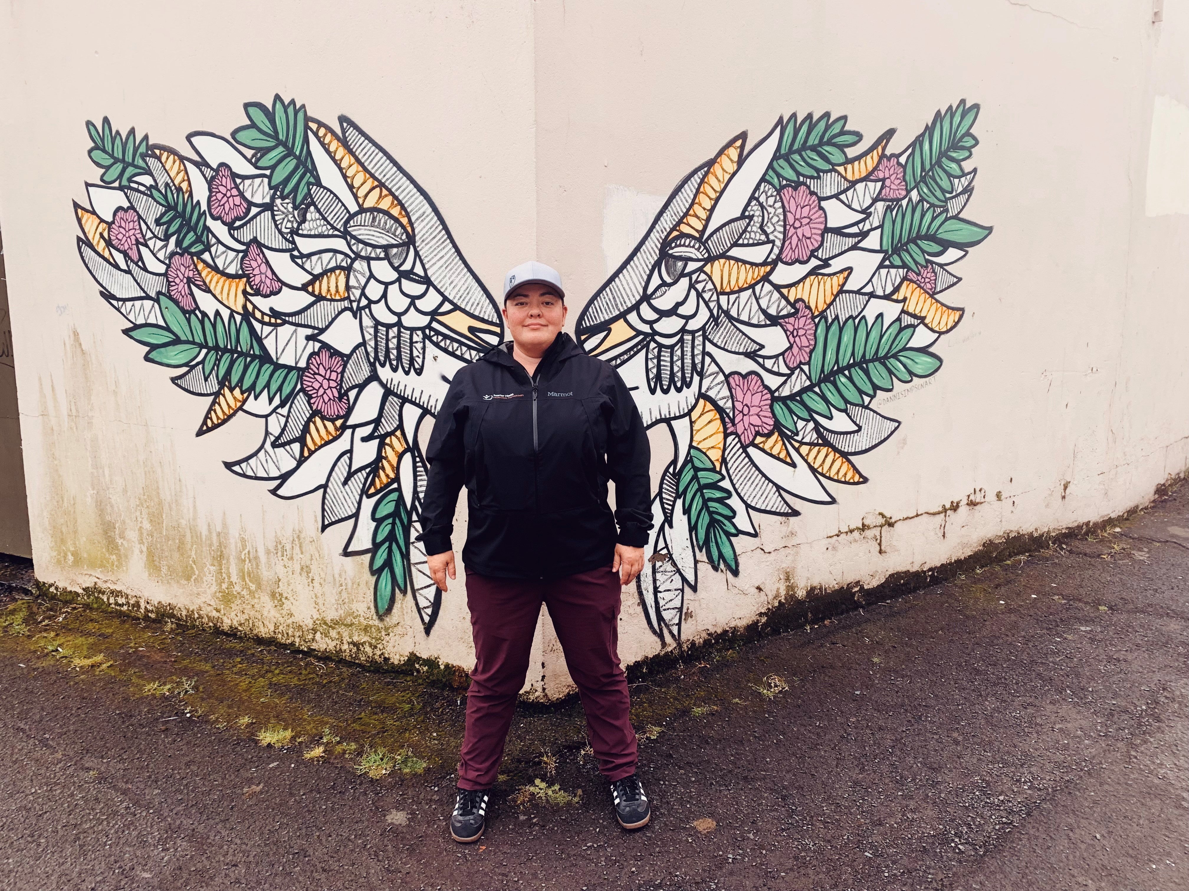 Person standing in front of wall artwork of wings on a while wall outdoors. 