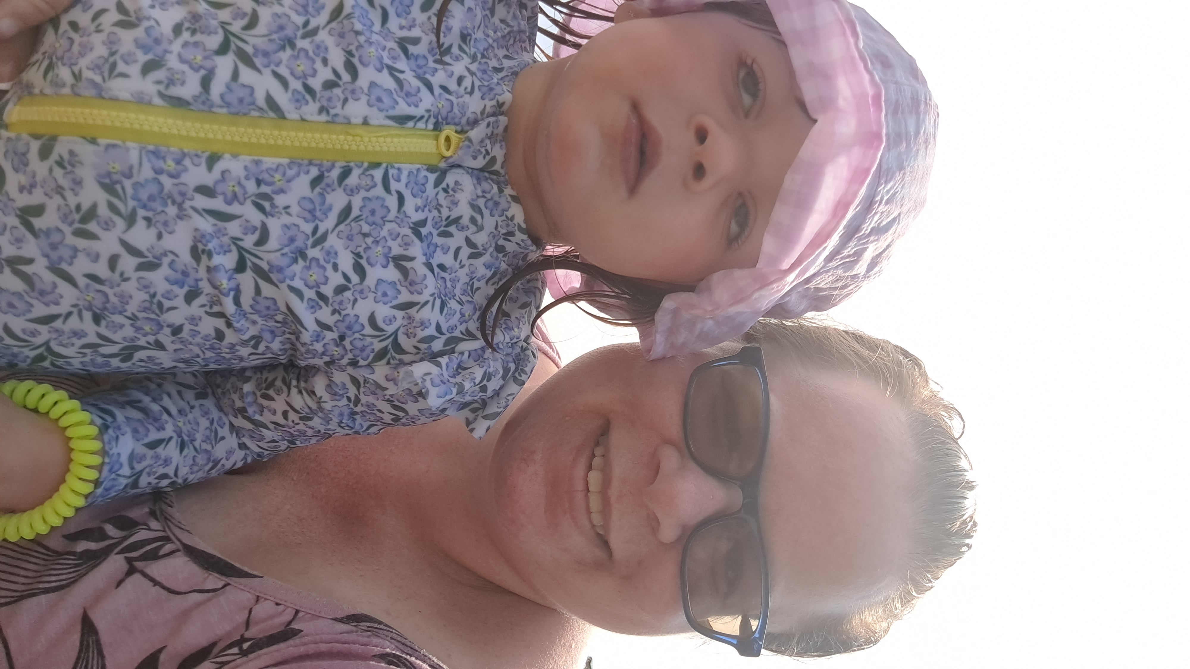 A selfie of a woman wearing sunglasses who has a young girl on her lap who is wearing a coat and hat.