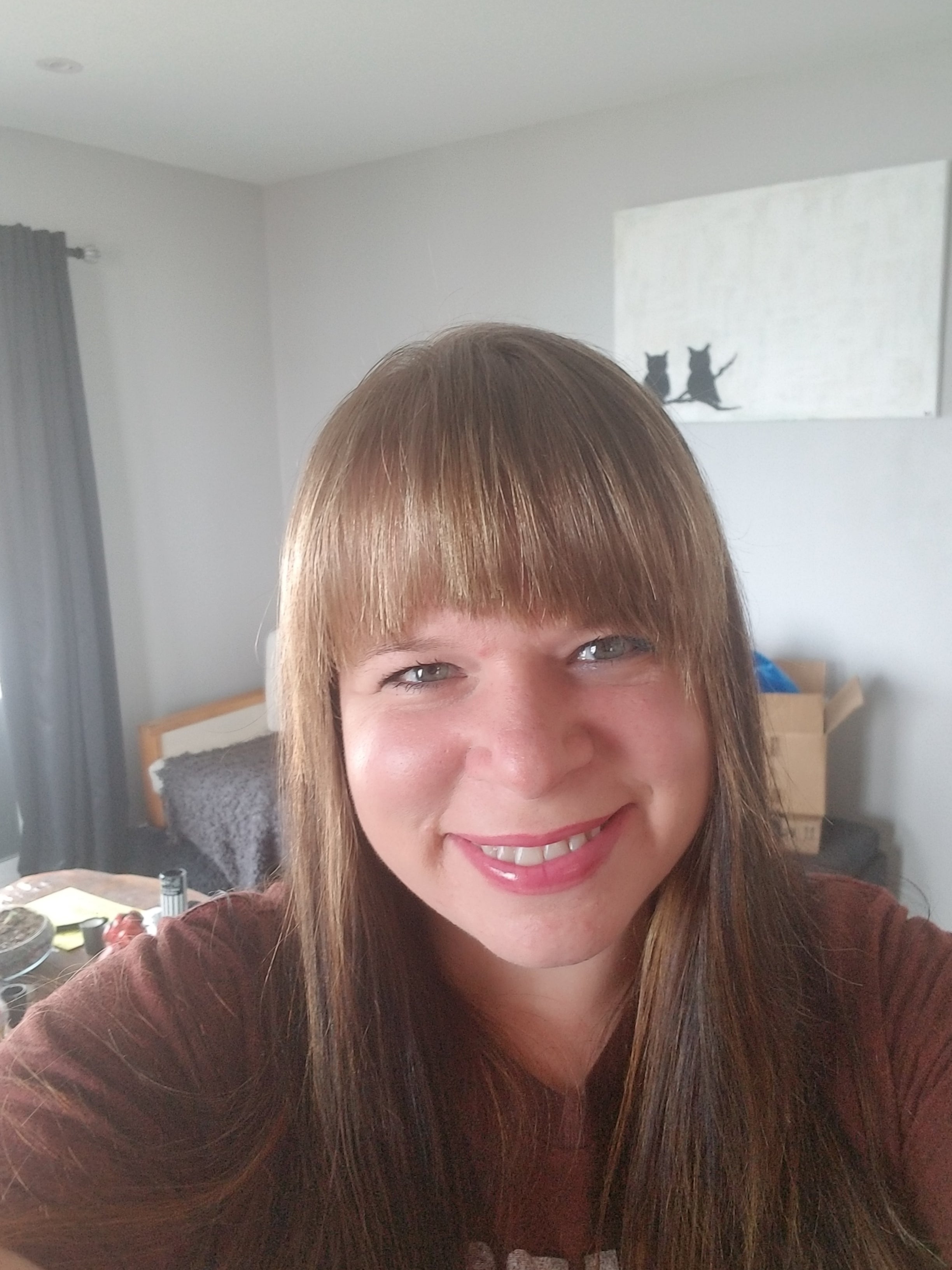 A selfie of a smiling woman with long, light brown hair who is wearing a maroon shirt.