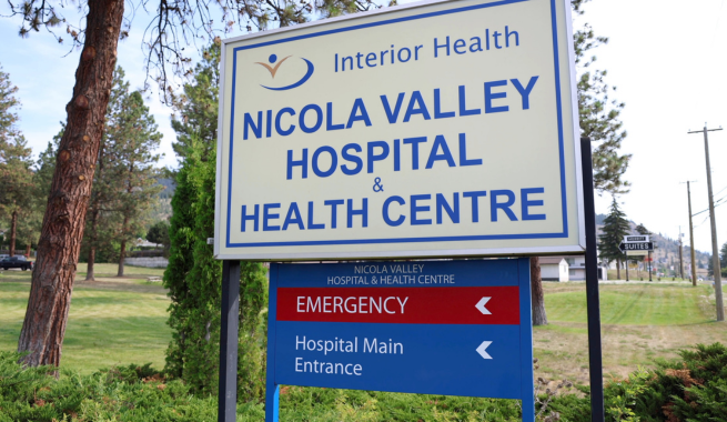 A sign with an Interior Health logo reading Nicola Valley Hospital, with arrows directing people left to Emergency and the Hospital Main Entrance.