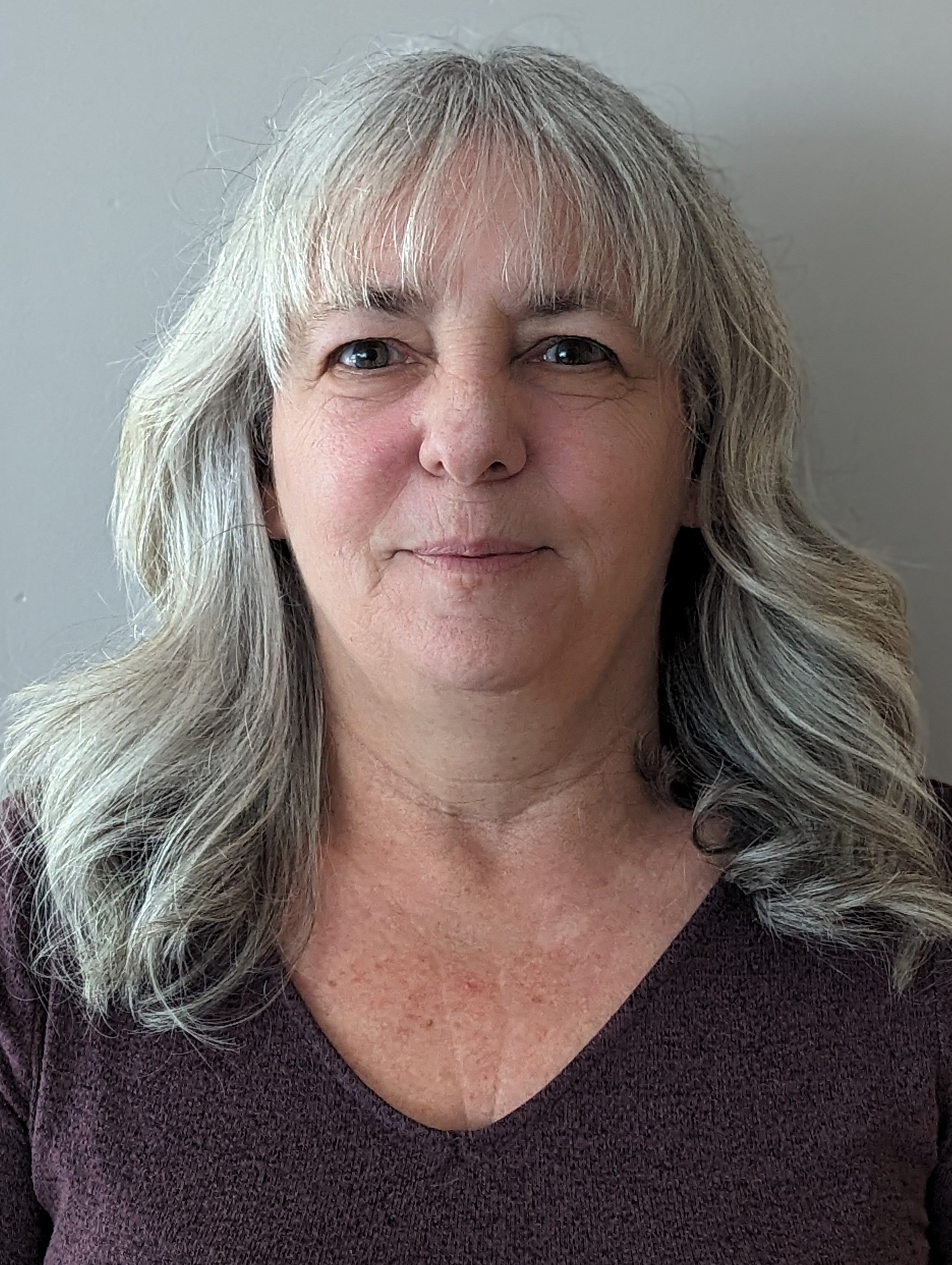 A woman with silver blond hair and brown shirt.