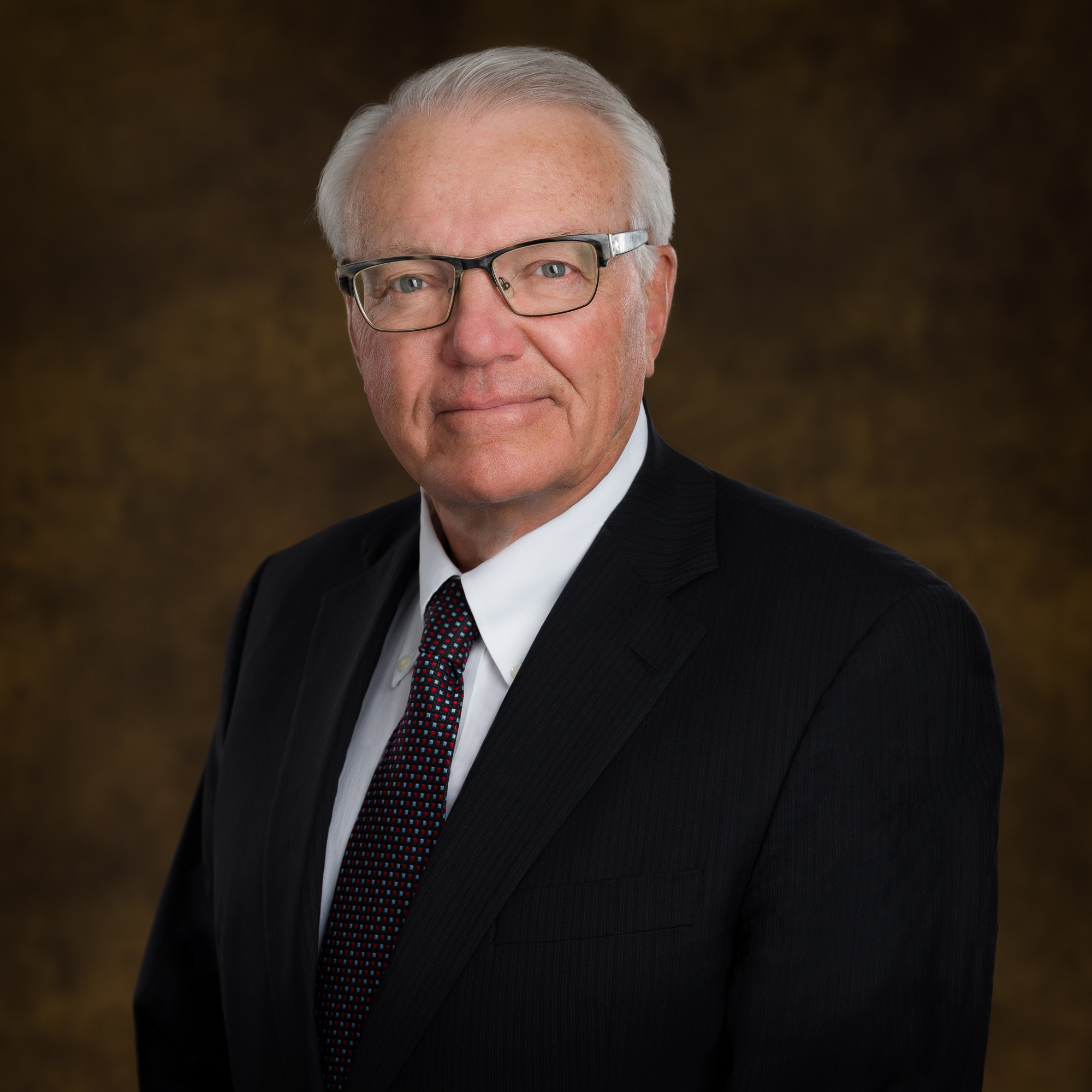 A profile photo of a middle aged man with silver hair and glasses wearing a business suit and tie.