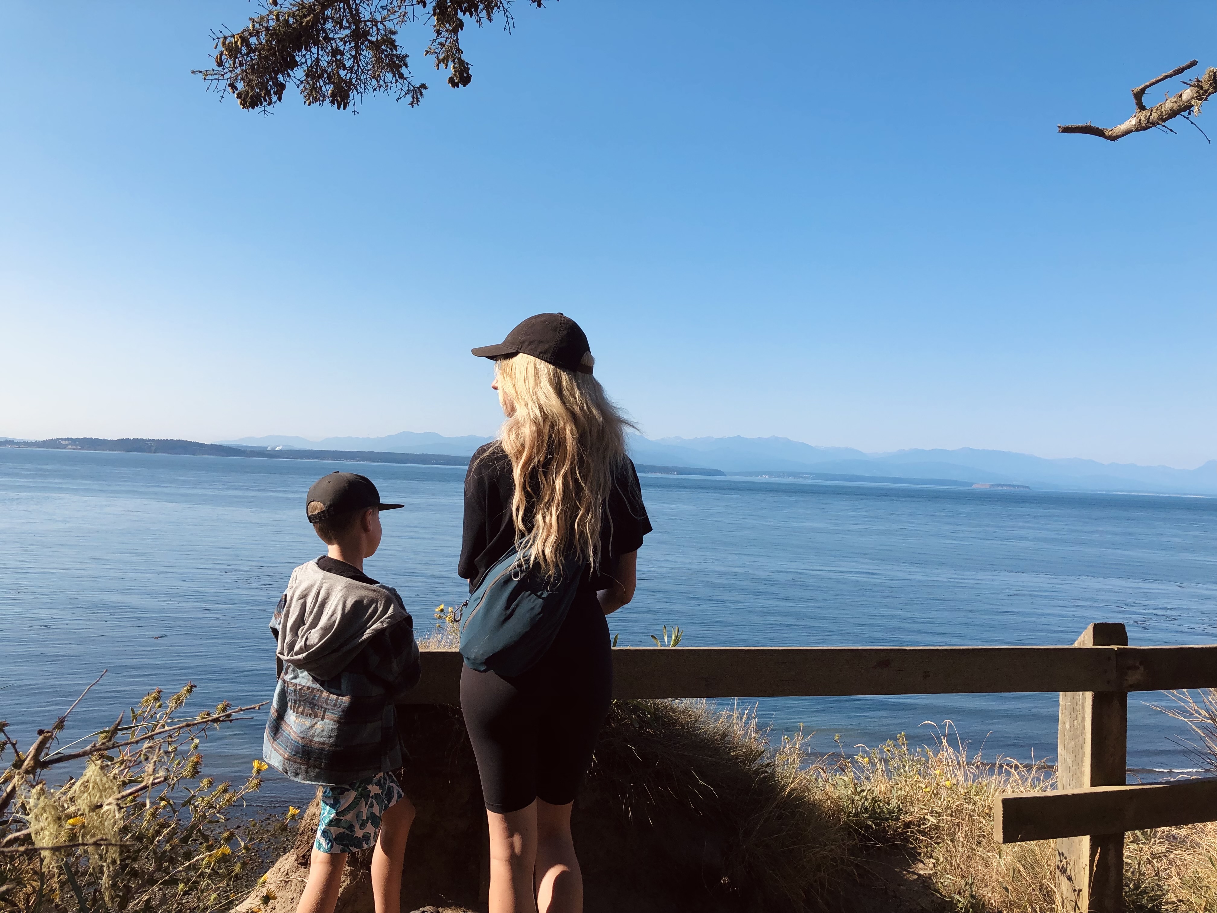 A blonde woman and her young son looking at the scenery at the top of a mountain hike checkpoint, facing away