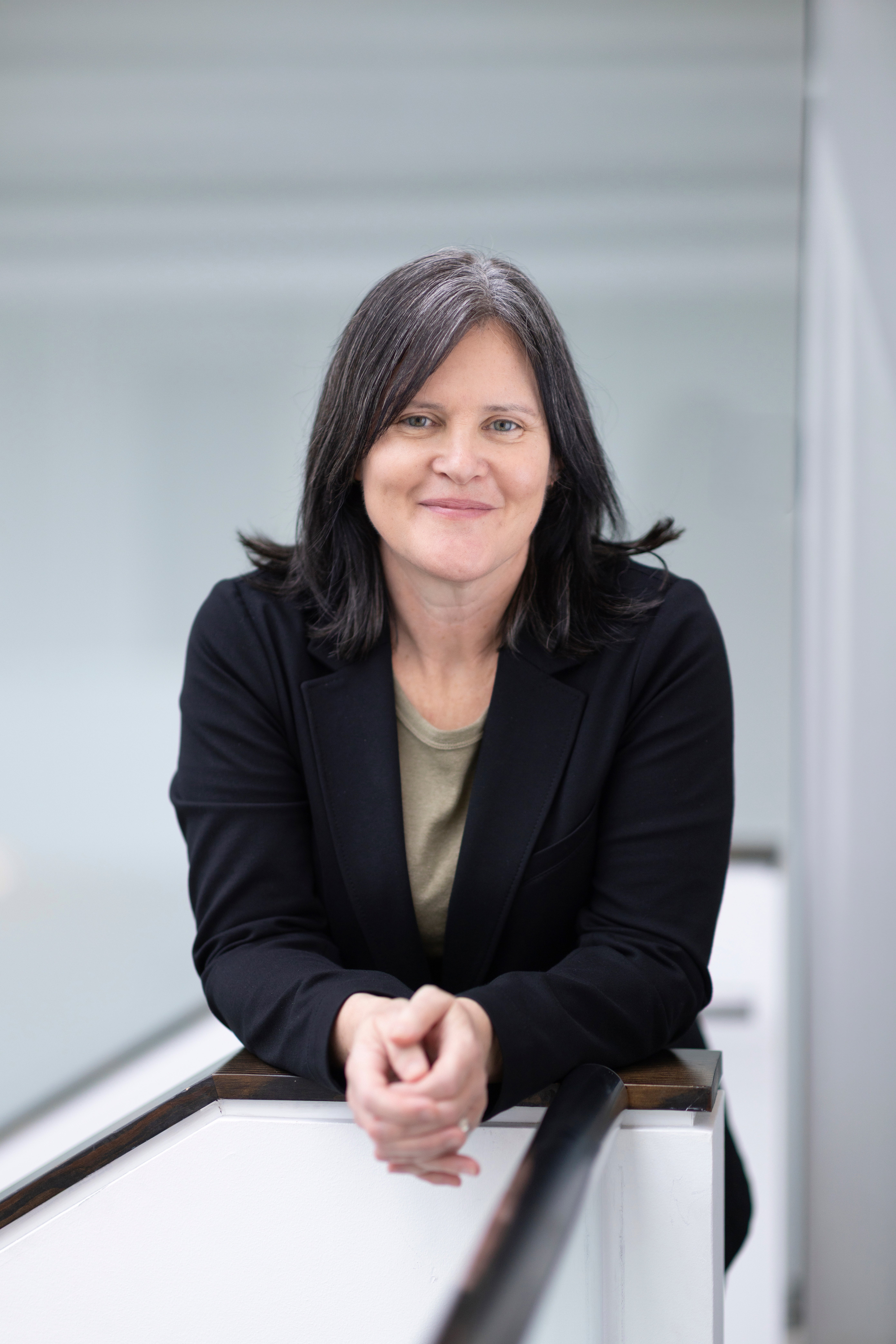 Profile shot of a smiling person with long black hair wearing a green shirt and black blazer.