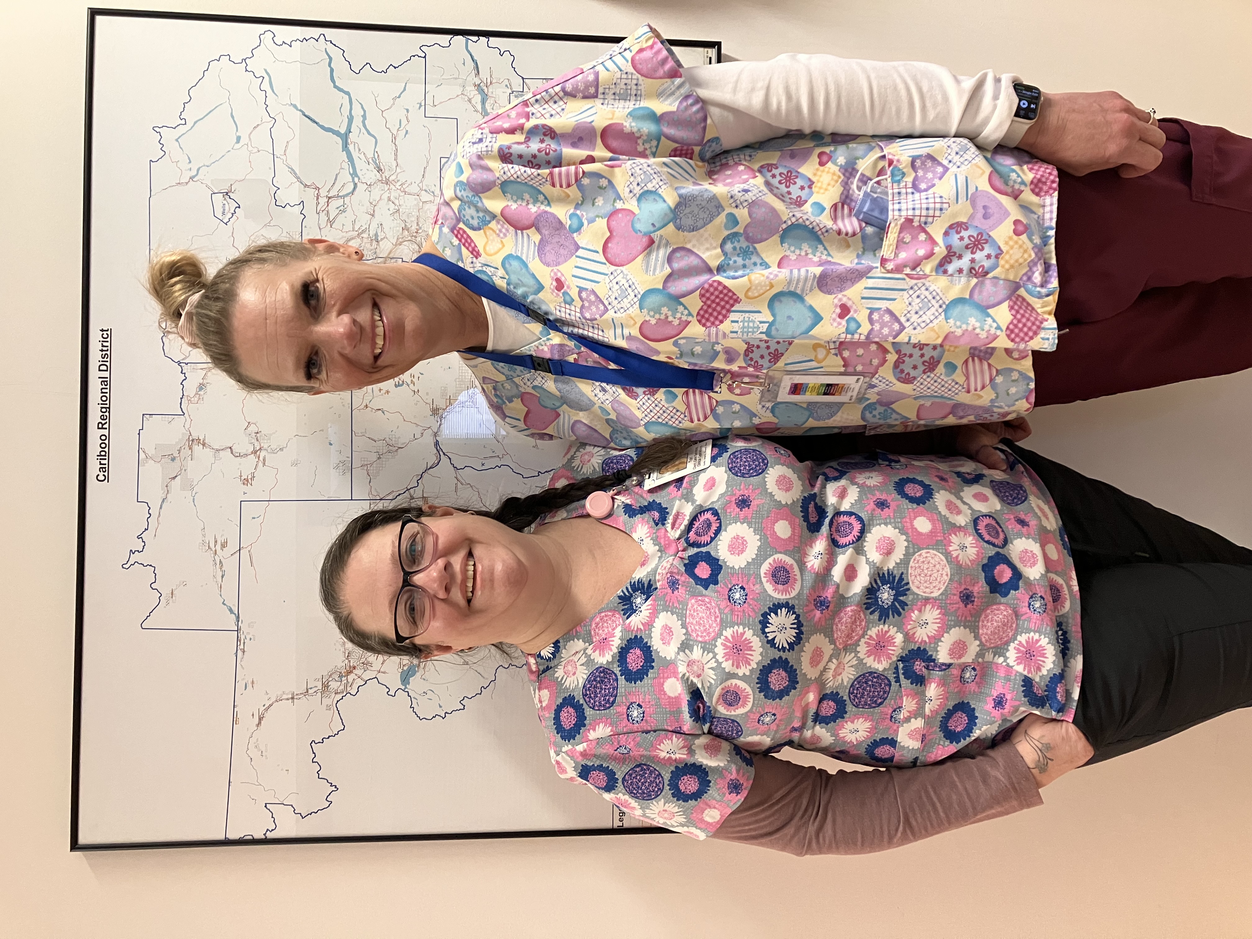Two women in colourful medical clothing stand in front of a map