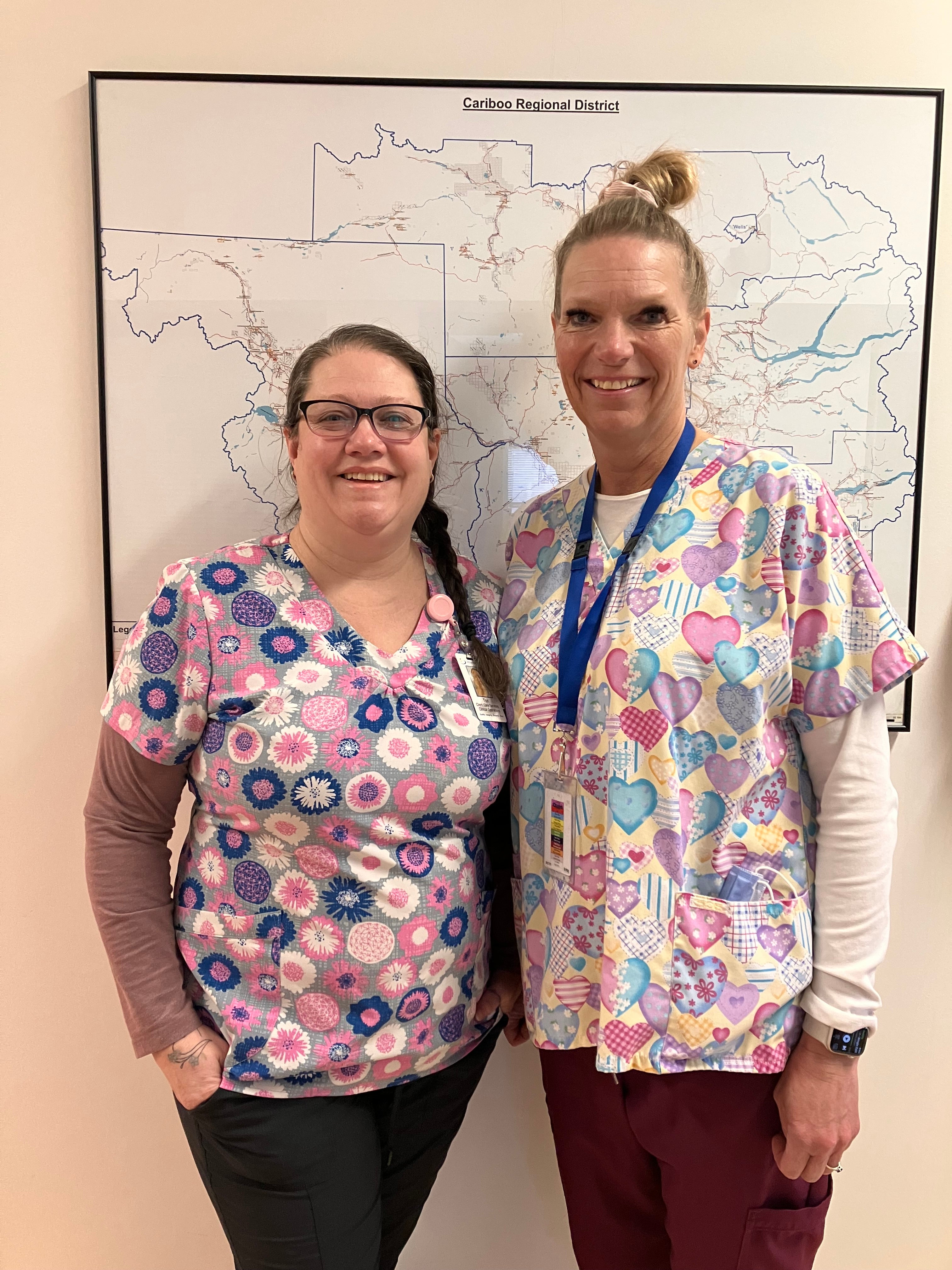 Two women in colourful medical clothing stand in front of a map