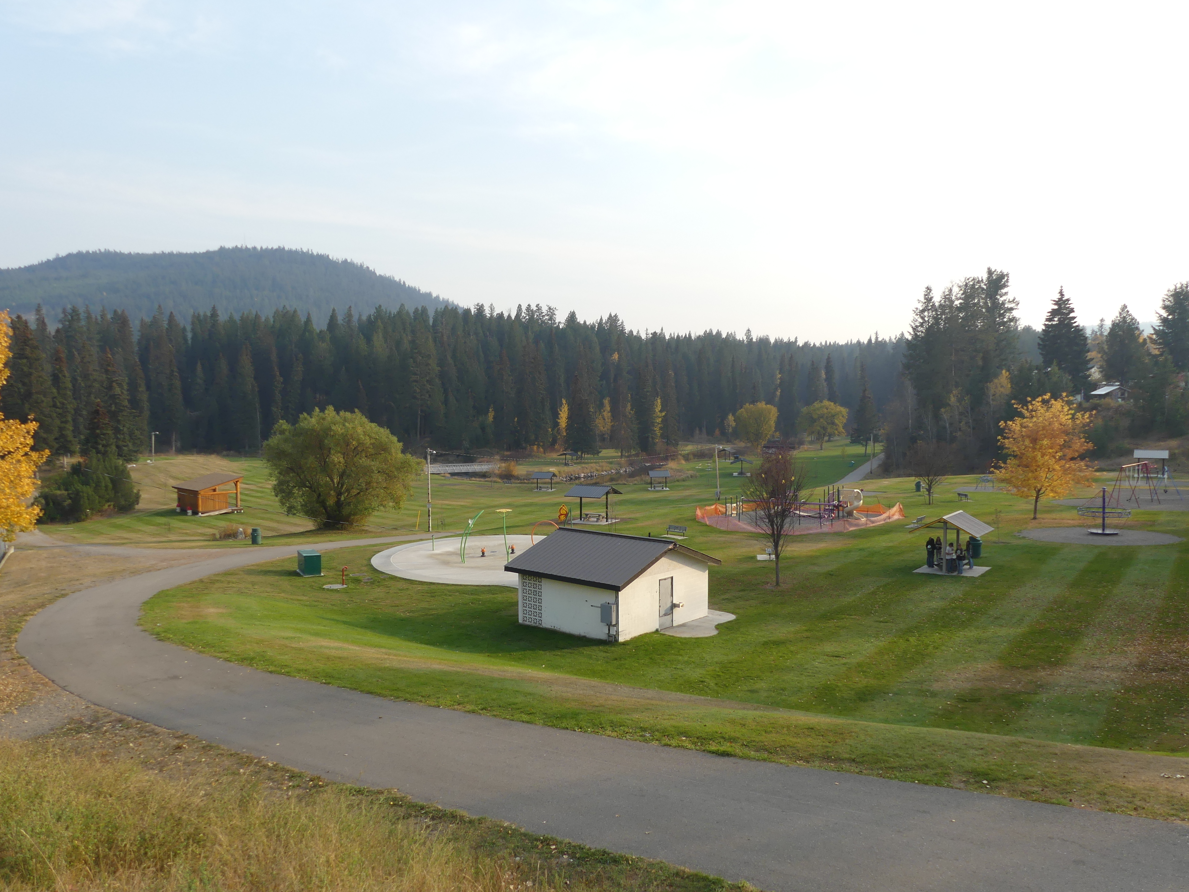 A park with green grass, trees and a mountain in the background, with playgrounds, washroom facilities and sports fields.