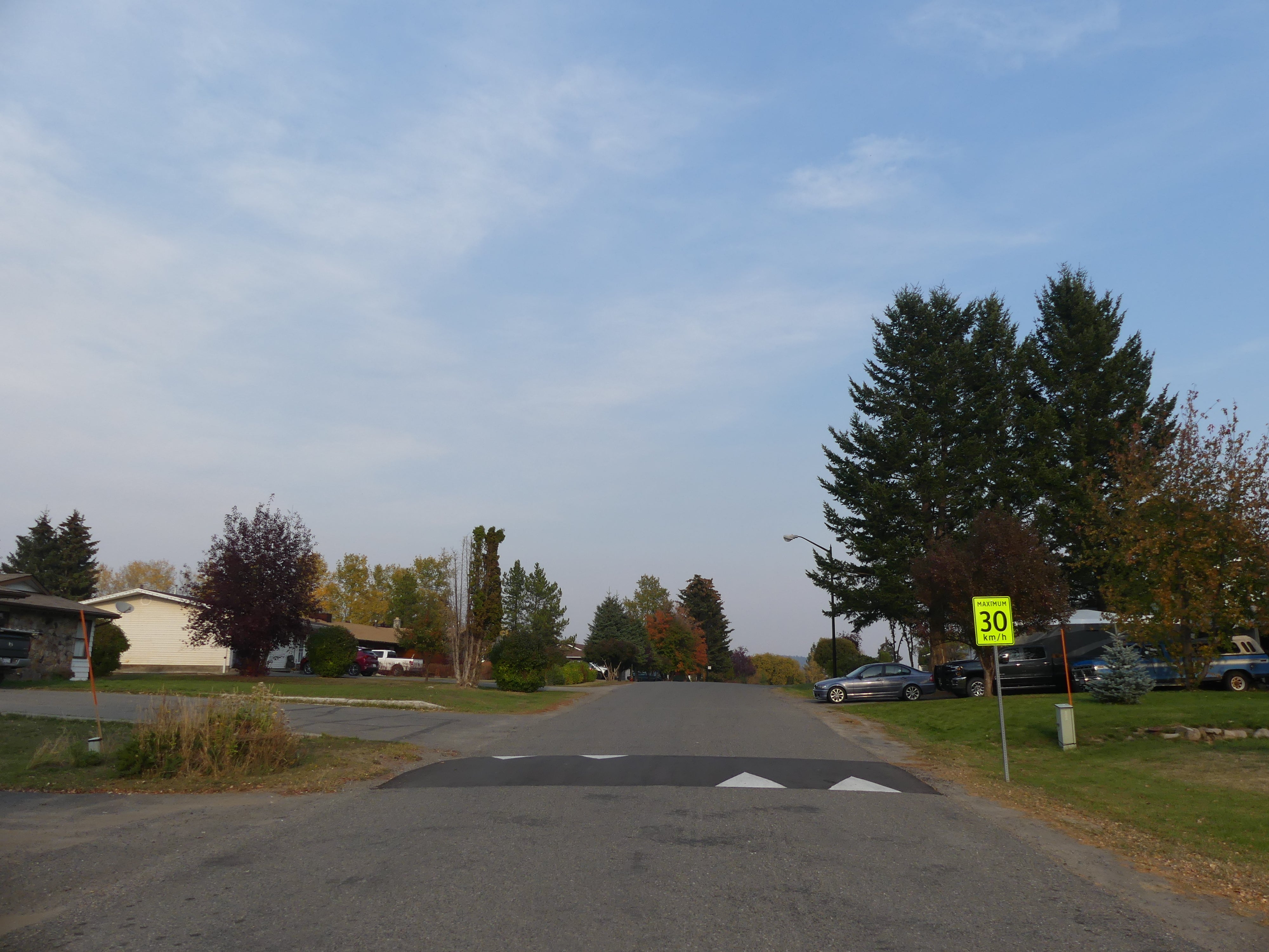 A speed bump on a narrow street, with a yellow sign that says "Maximum 30 km/h" to the right, and houses on either side.