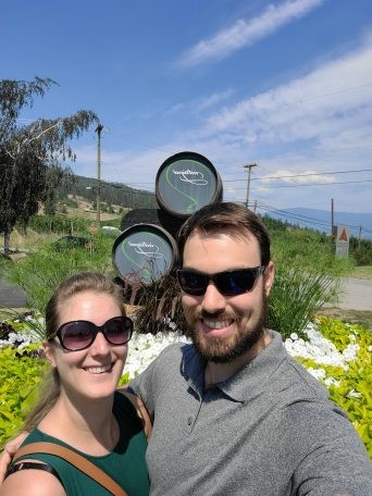 A selfie photo of a woman, left and man in front of wine barrels