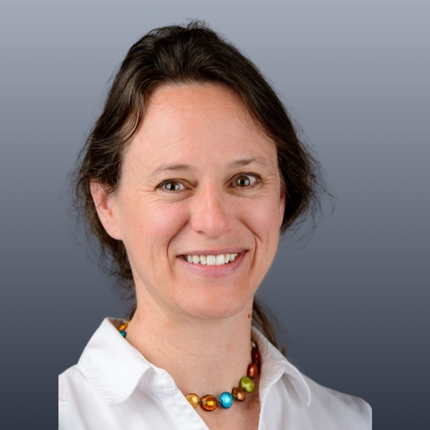  A headshot of a person wearing a white collared shirt and a necklace with colourful stones. 