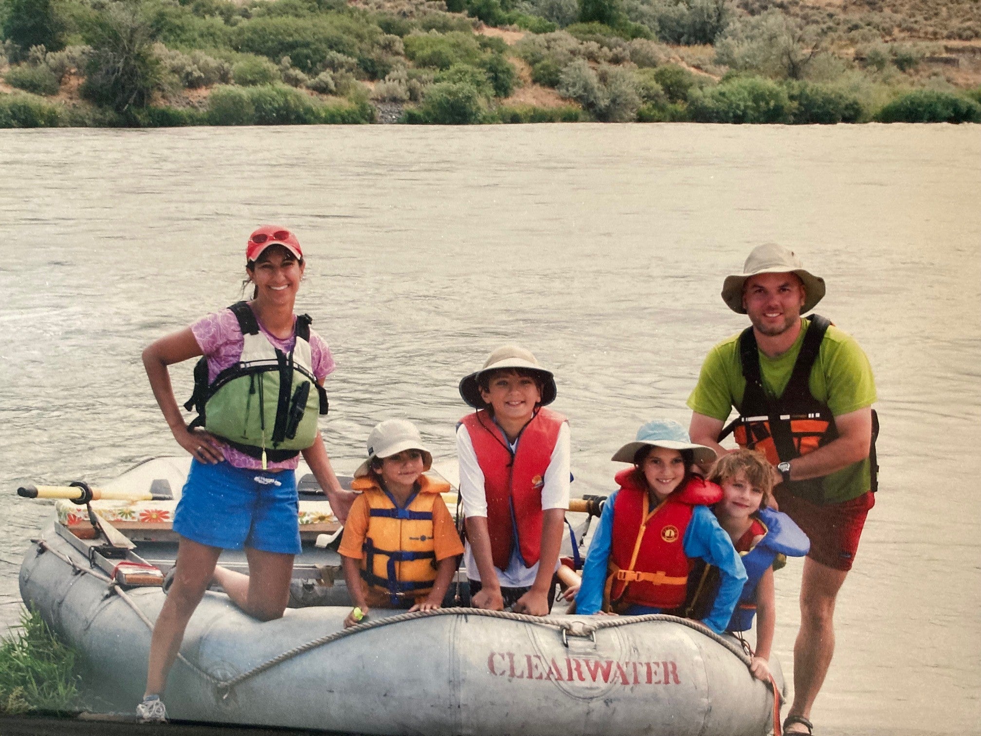 Family wearing lifeboat jackets in dinghy on river.