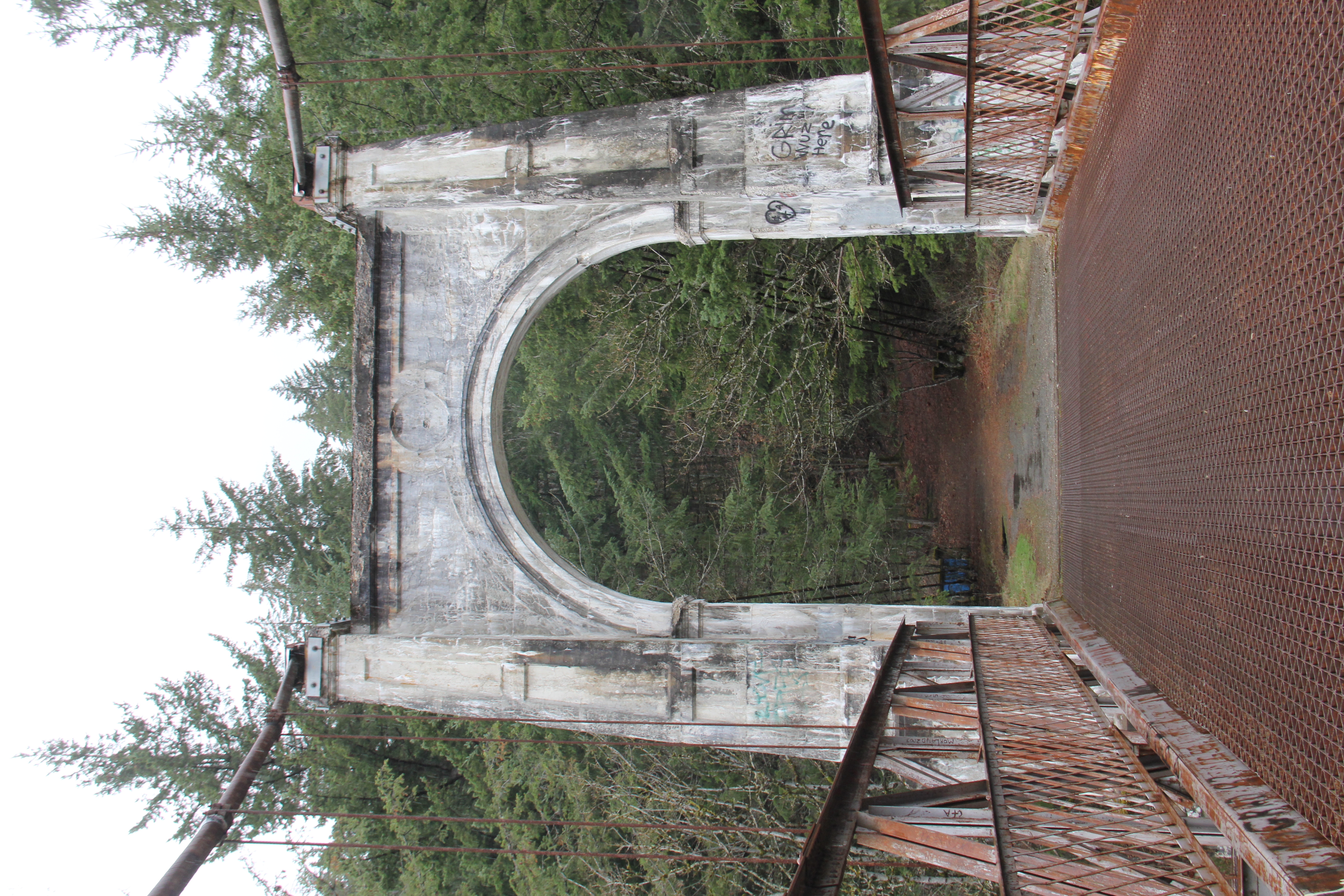 A bridge with a large supporting white arch leads into a forested area.
