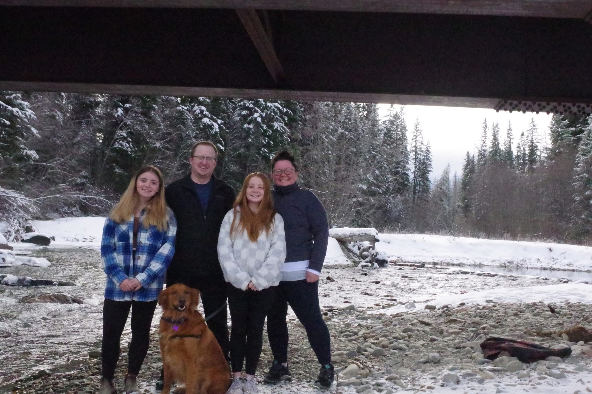 A family of four standing outside with their dog in winter under a bridge.