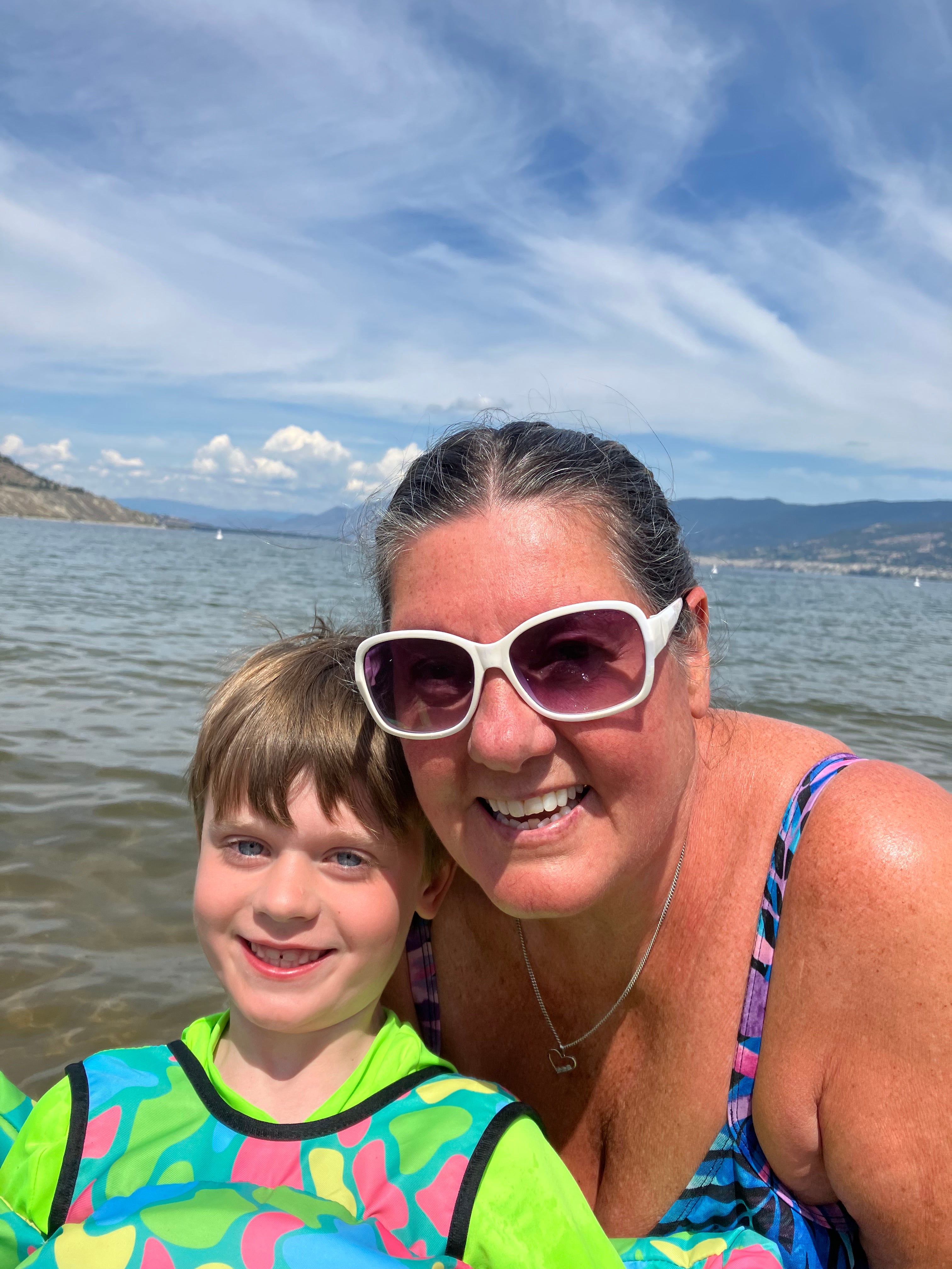 A woman with a child in brightly coloured swim gear in a lake. 