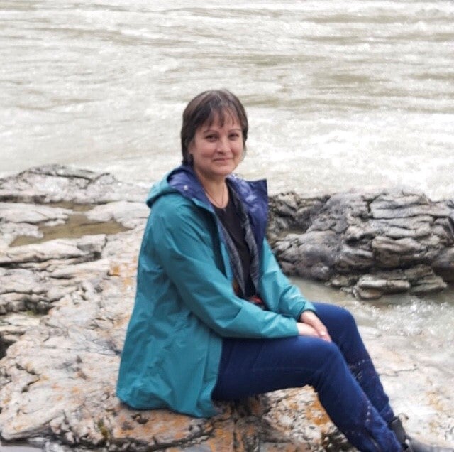 A woman sitting on a rock near the edge of a lake.