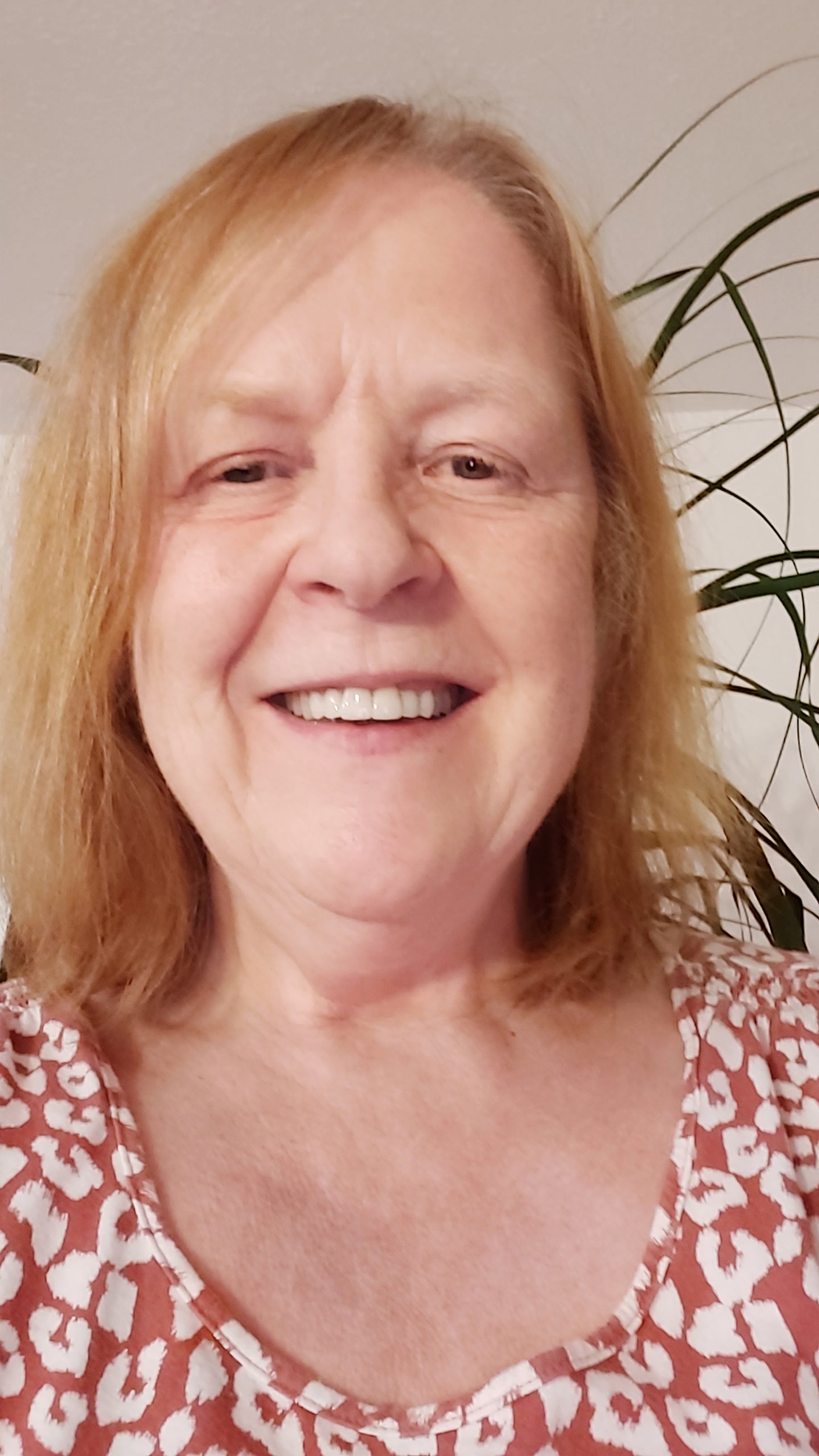 A selfie light-skinned woman with medium long red-blonde hair, wearing a red and white animal print shirt.