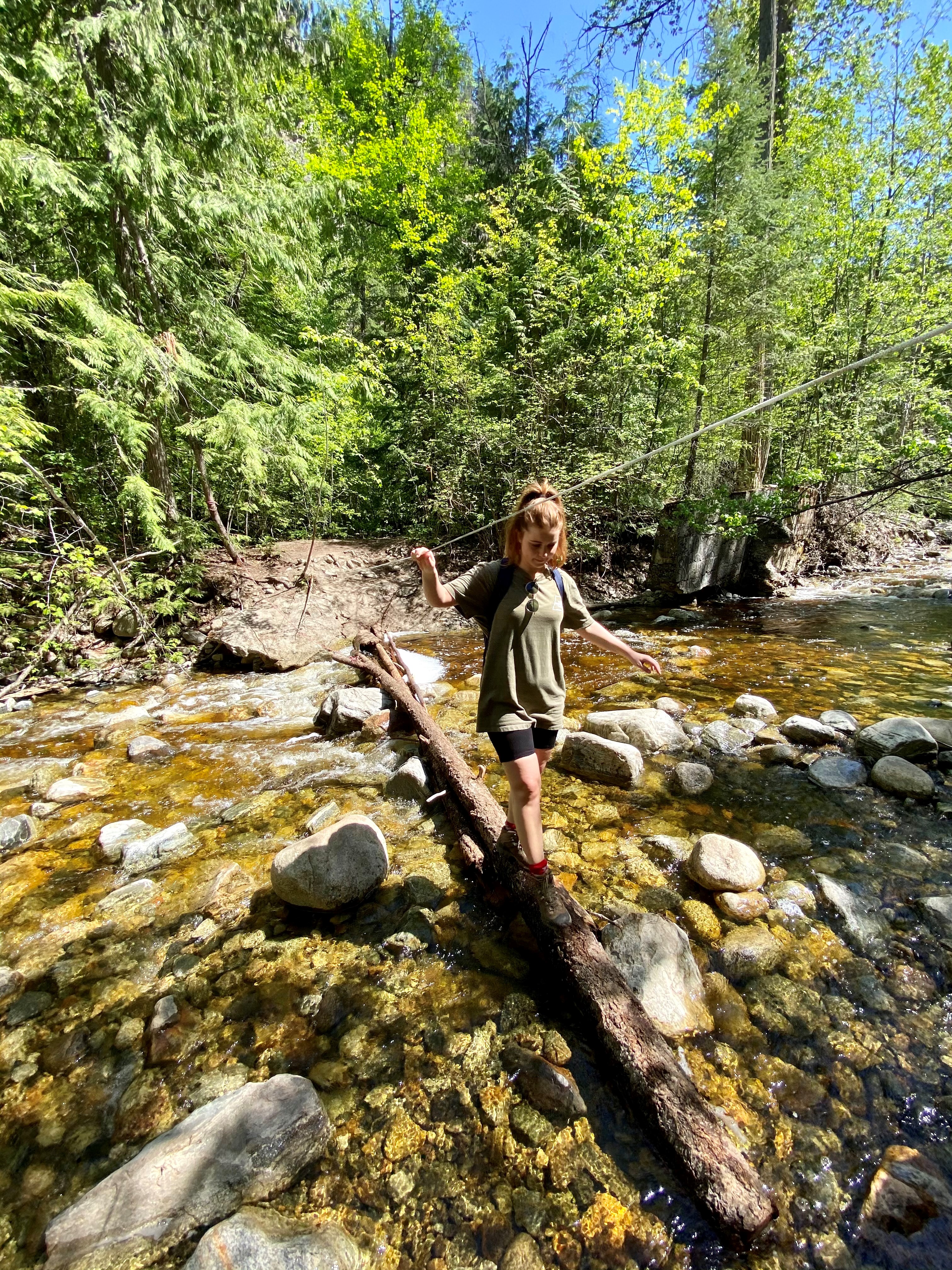 Young woman crossing a shallow stream by walking across a fallen tree.