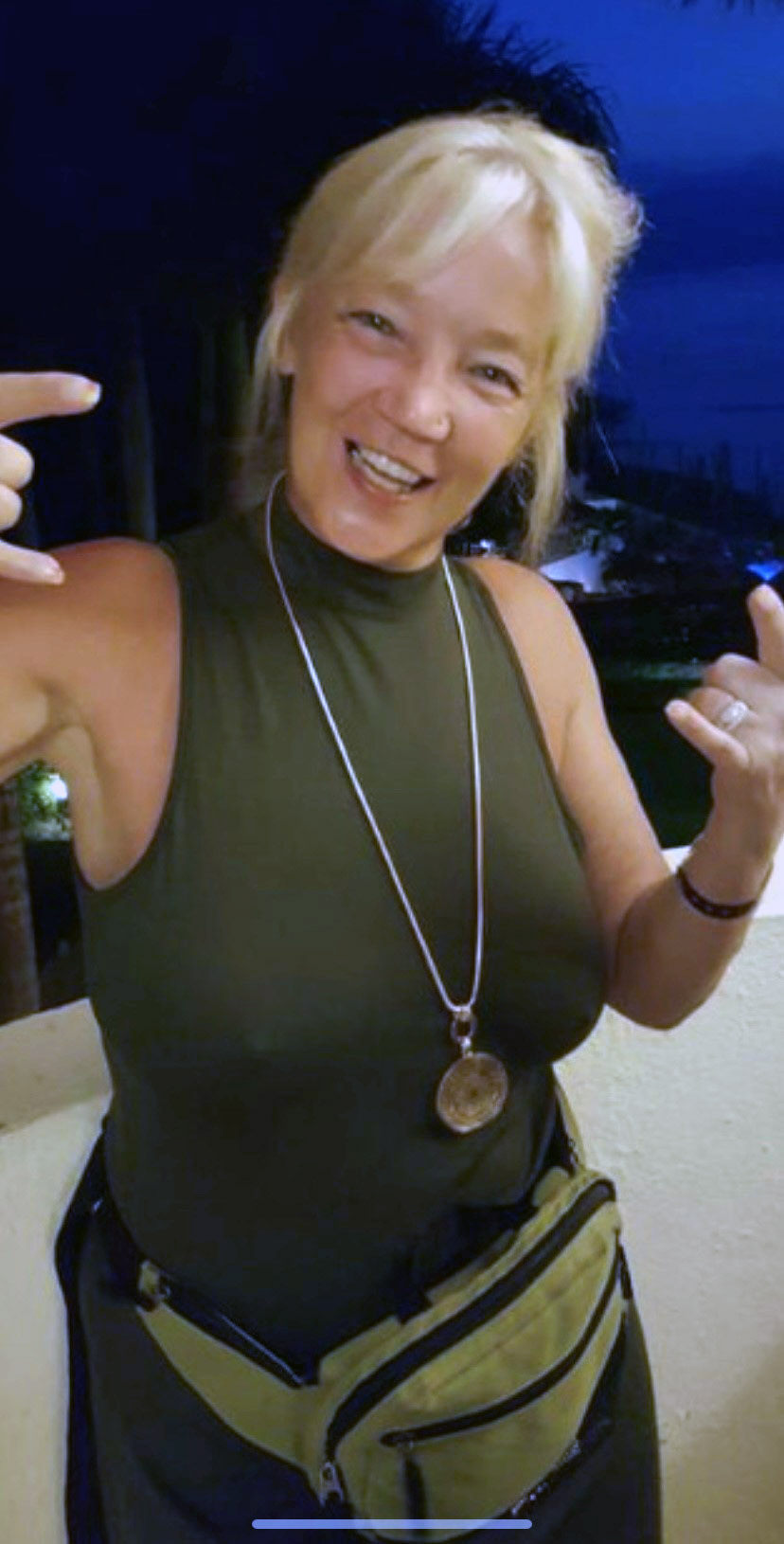 A woman with blonde hair wearing a black sleeveless shirt, black pants and a green fanny pack.