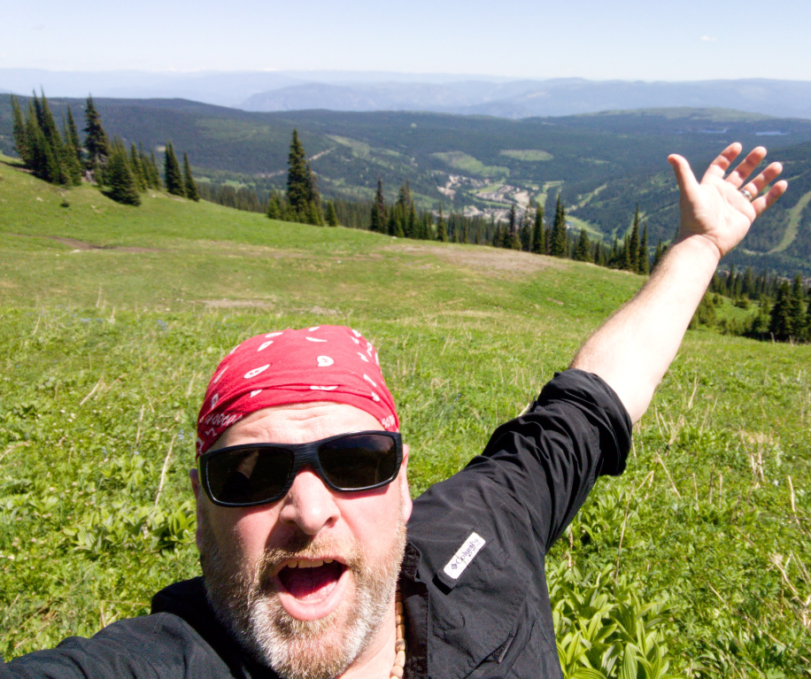 A selfie of a man on a hill with green landscape in the background 