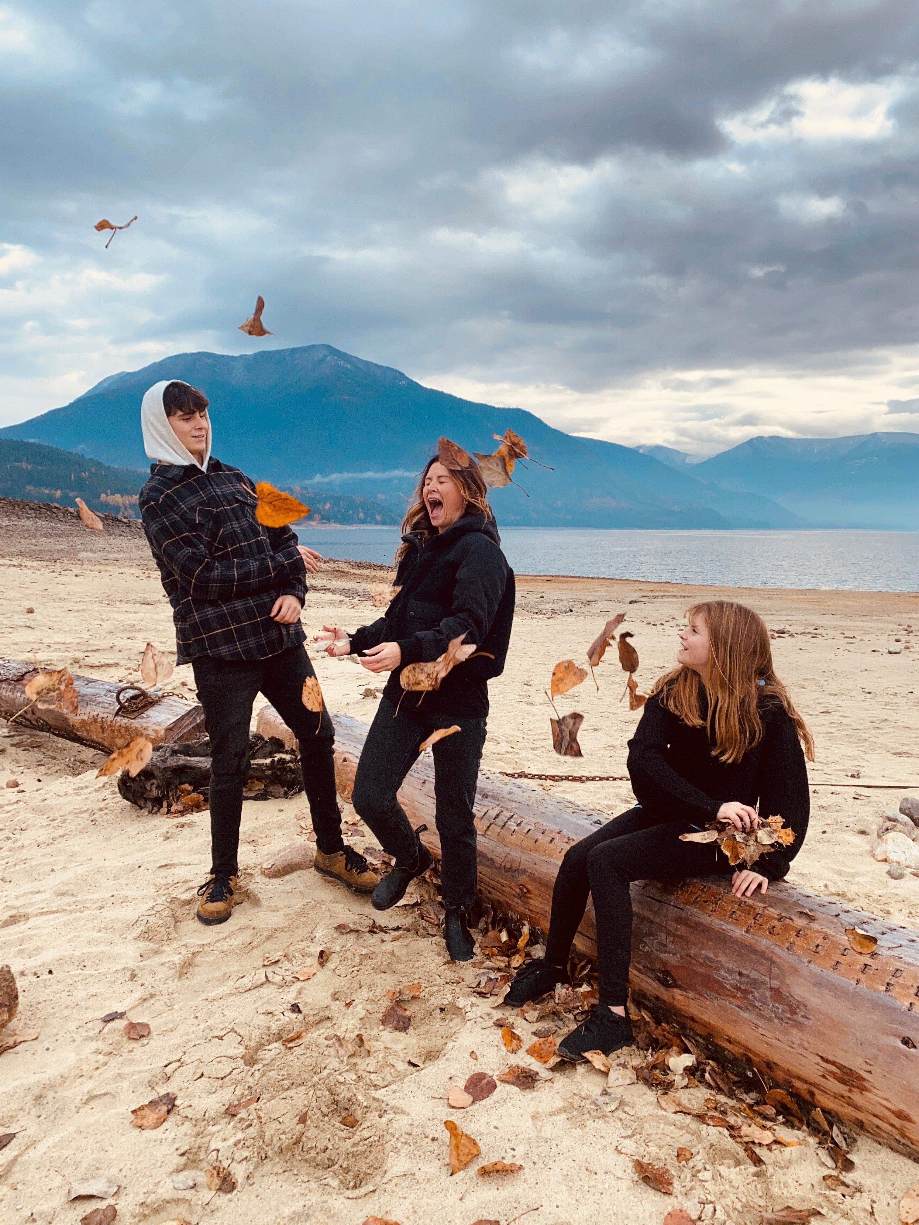 Three people are at a beach playing with leaves.