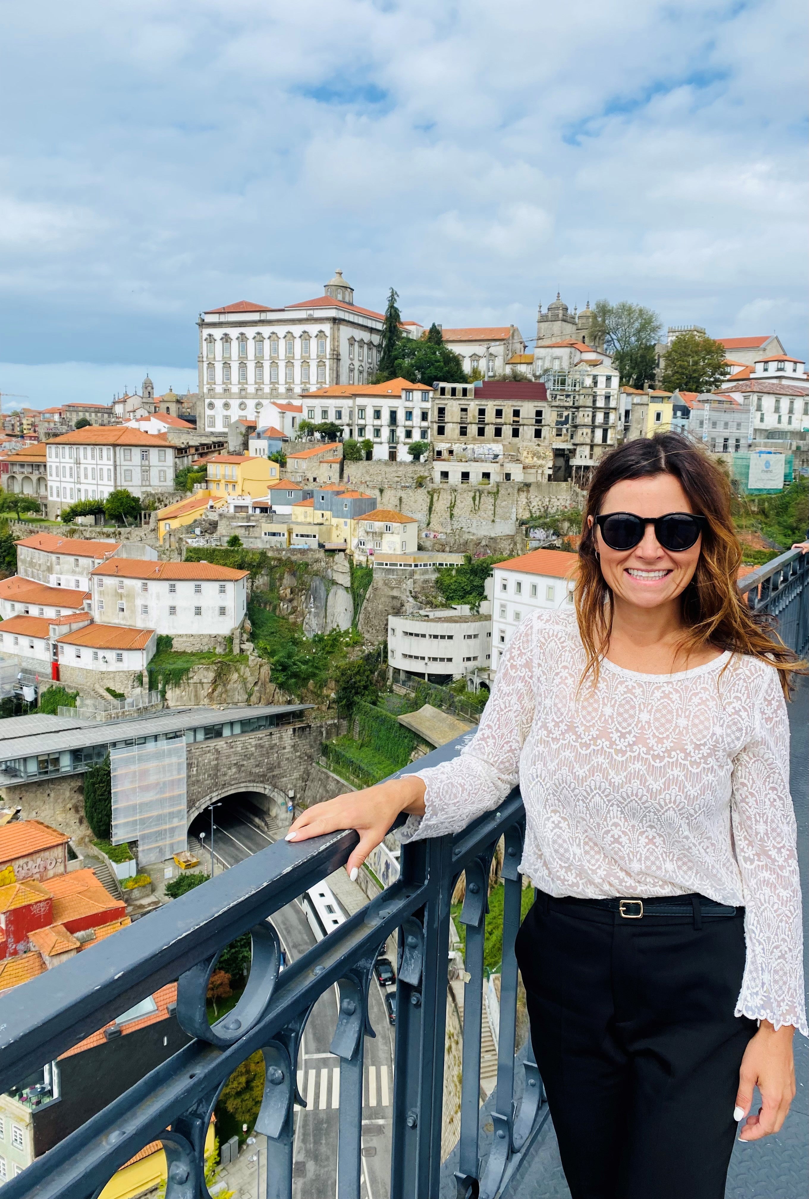 A woman stands in front of a railing looking over a city.