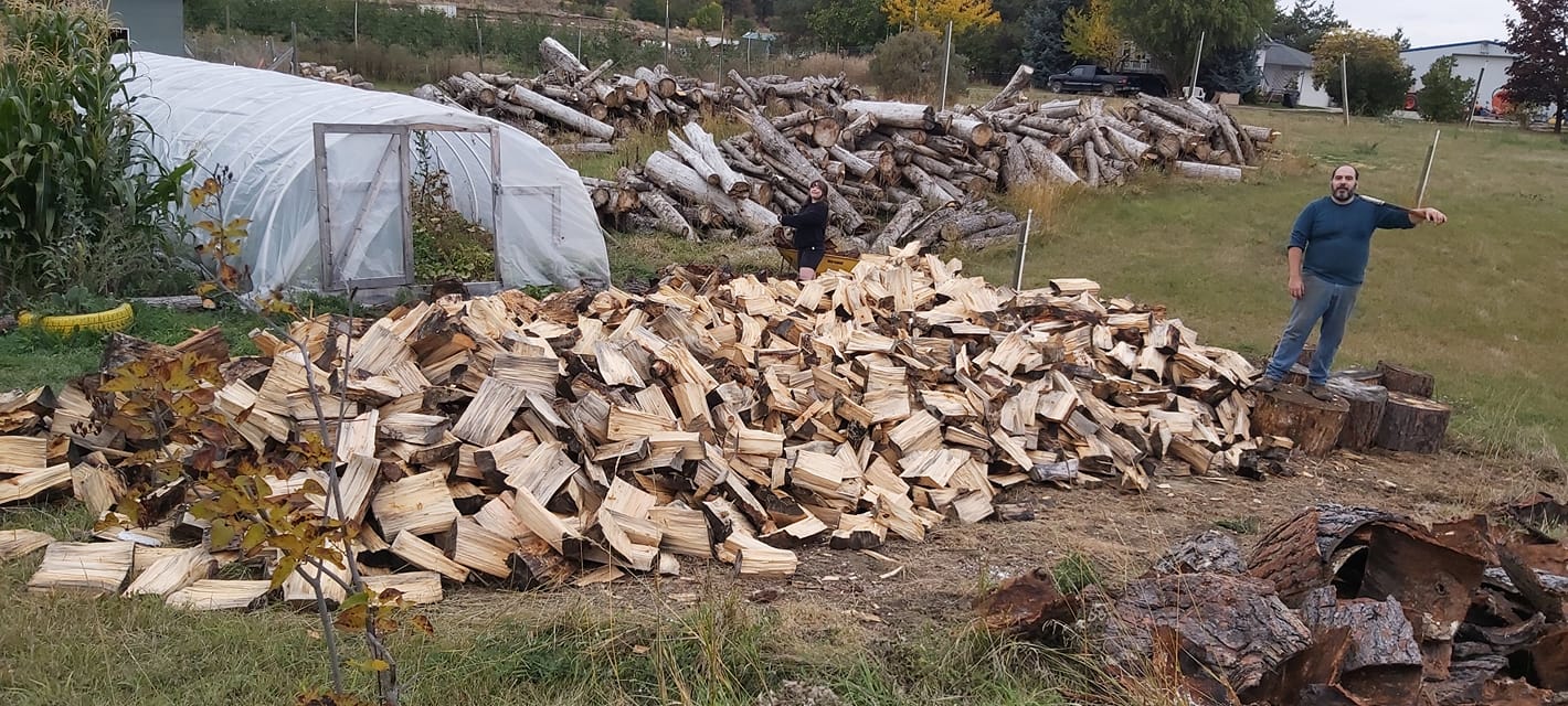 Man standing beside a large pile of chopped firewood.