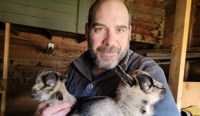 Man with beard holding 2 baby goats.