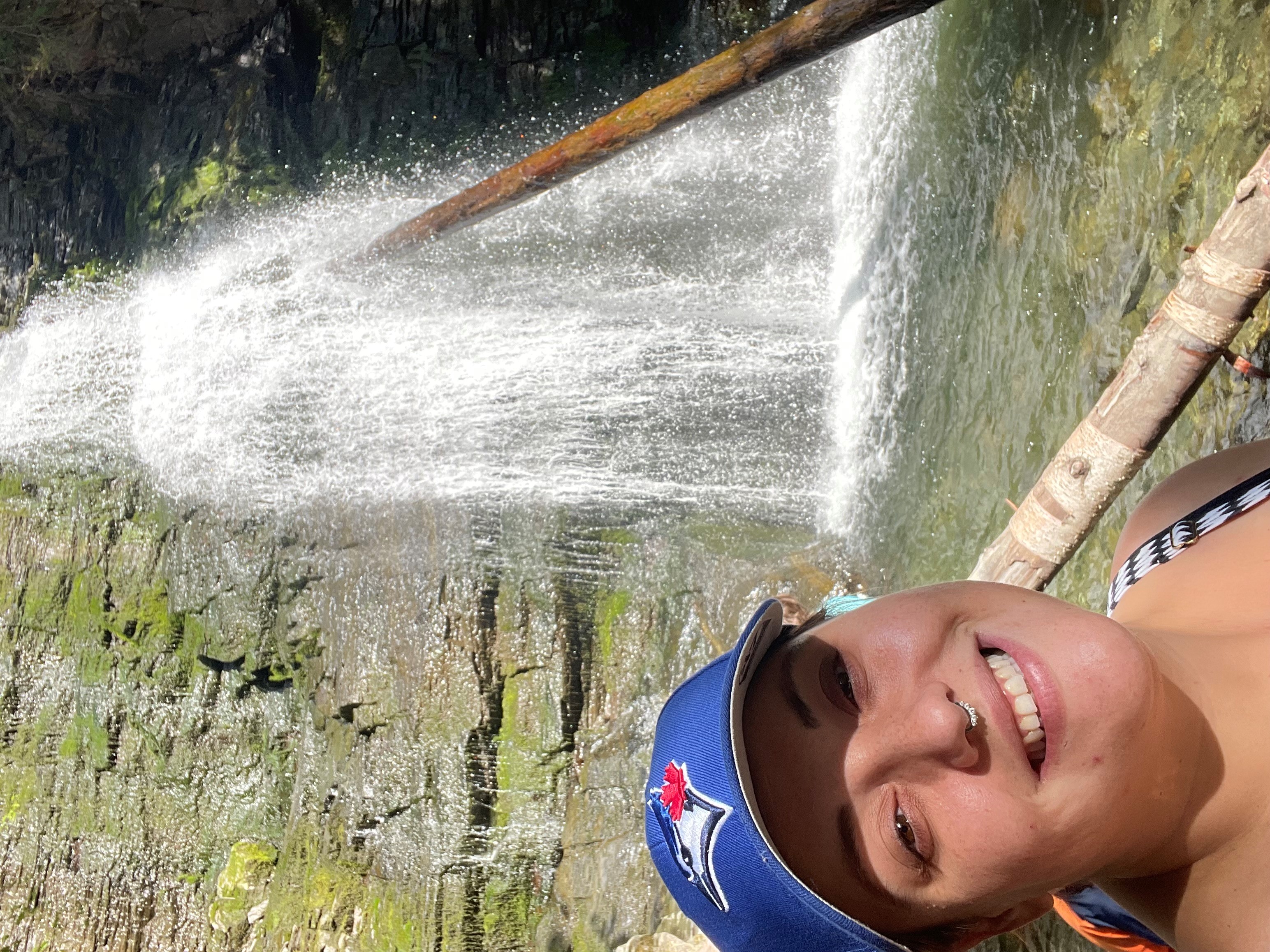 A woman wearing a Blue Jays ball cap stands near a waterfall.