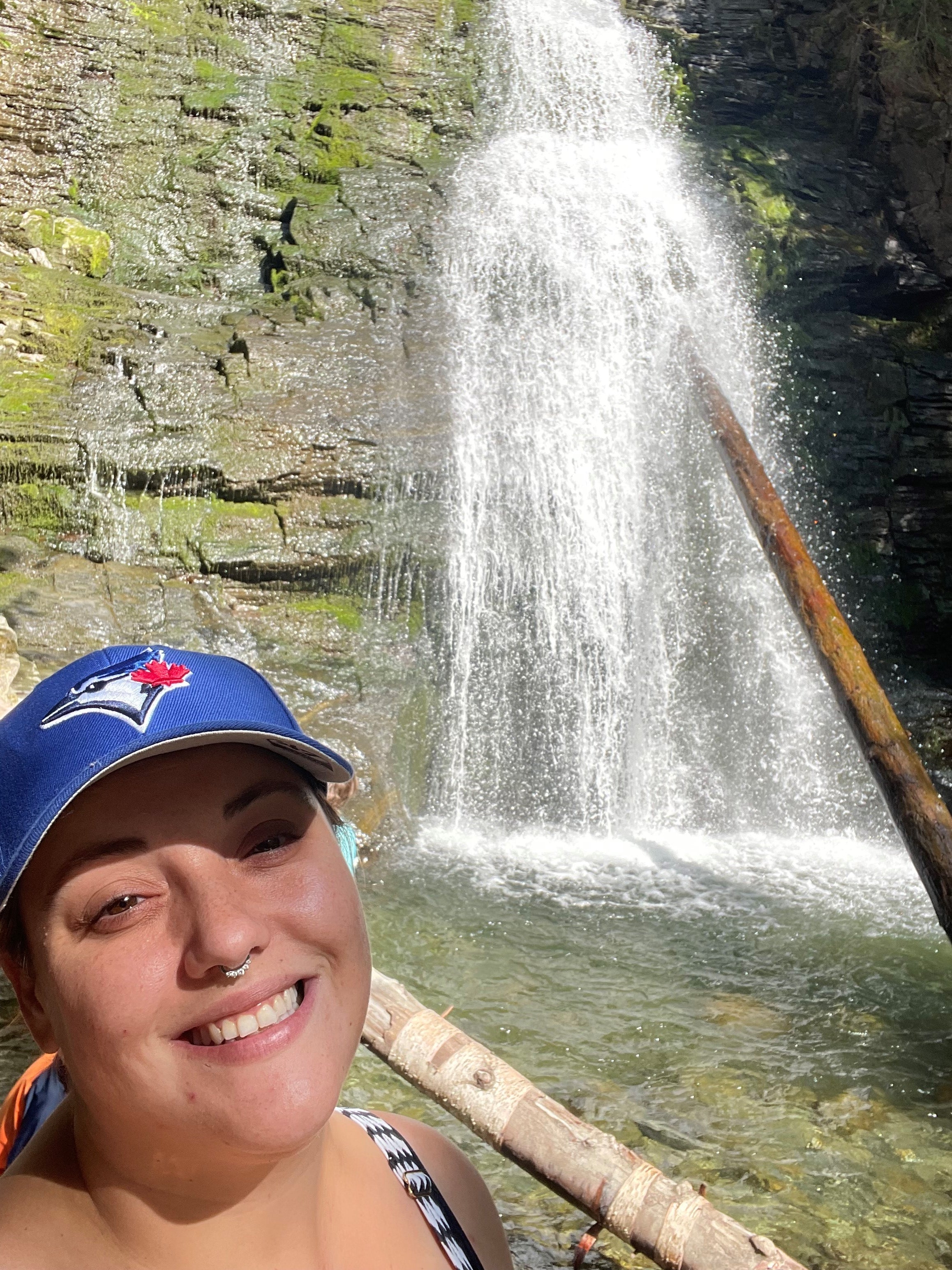 A woman wearing a Blue Jays ball cap stands near a waterfall.