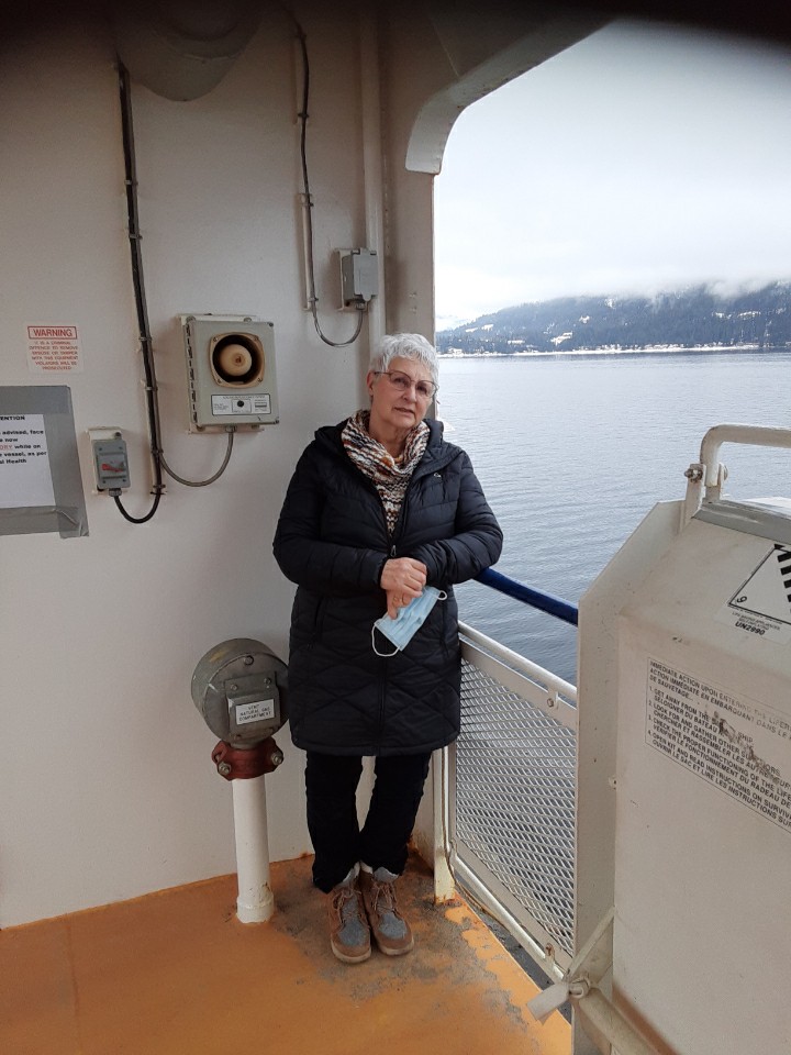 White-haired woman wearing glasses and a coat, leaning on railing of a ferry boat.