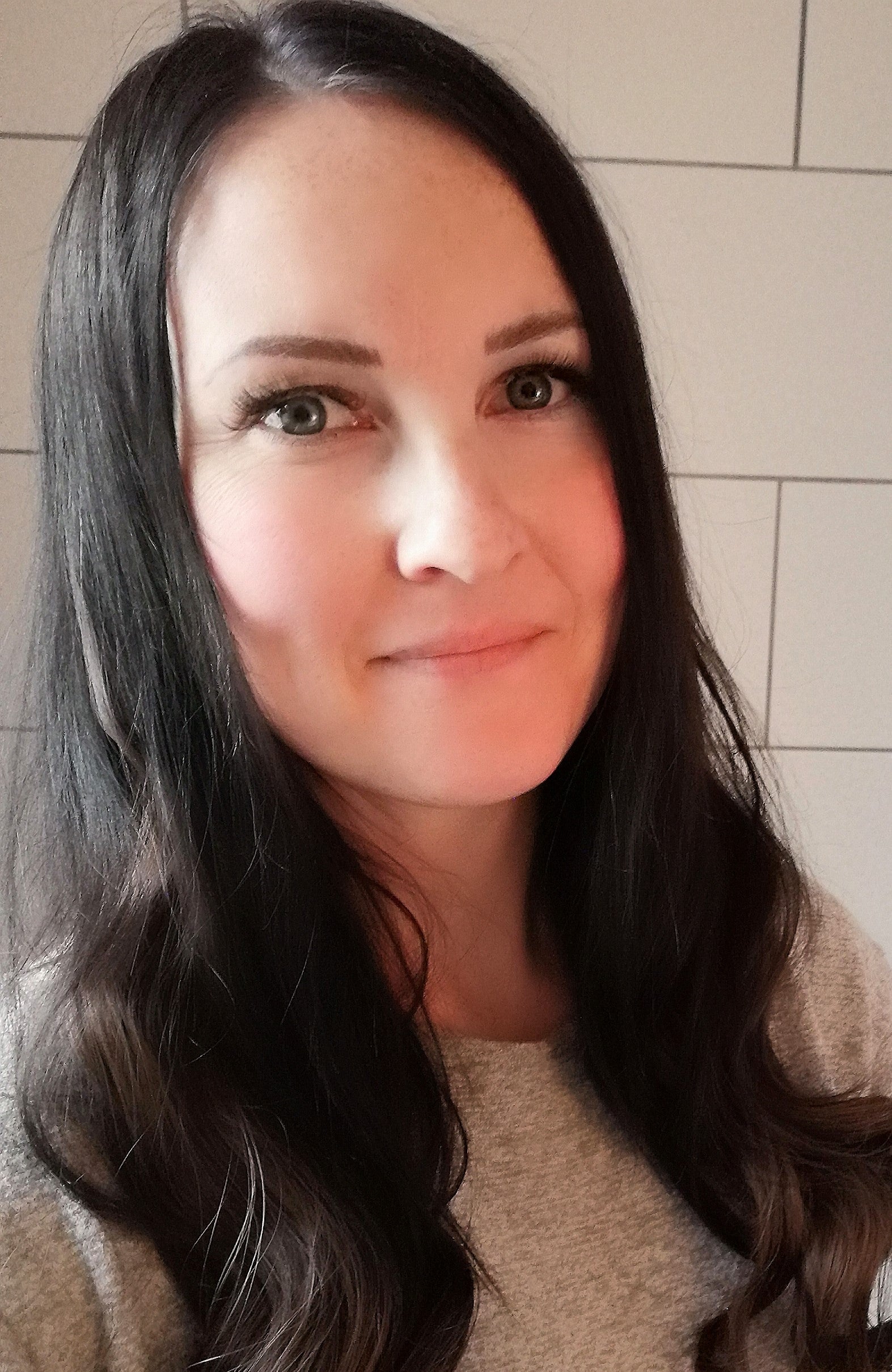 A woman with long brown hair smiles as she looks at the camera. 