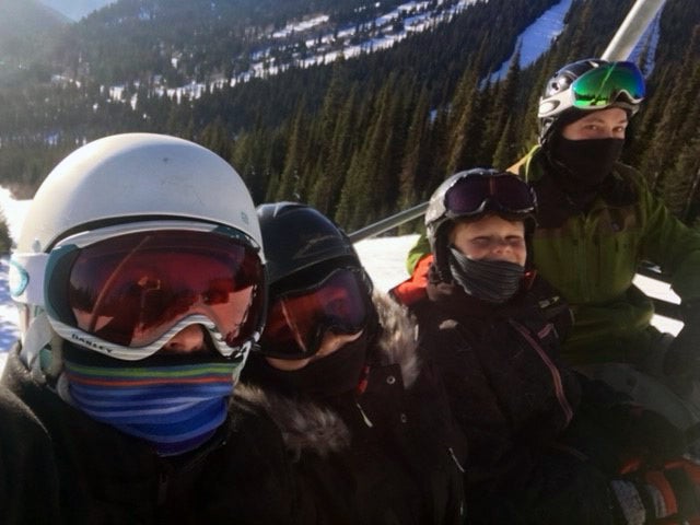 Four people in skiing gear in front of a snowy mountain covered in evergreen trees.