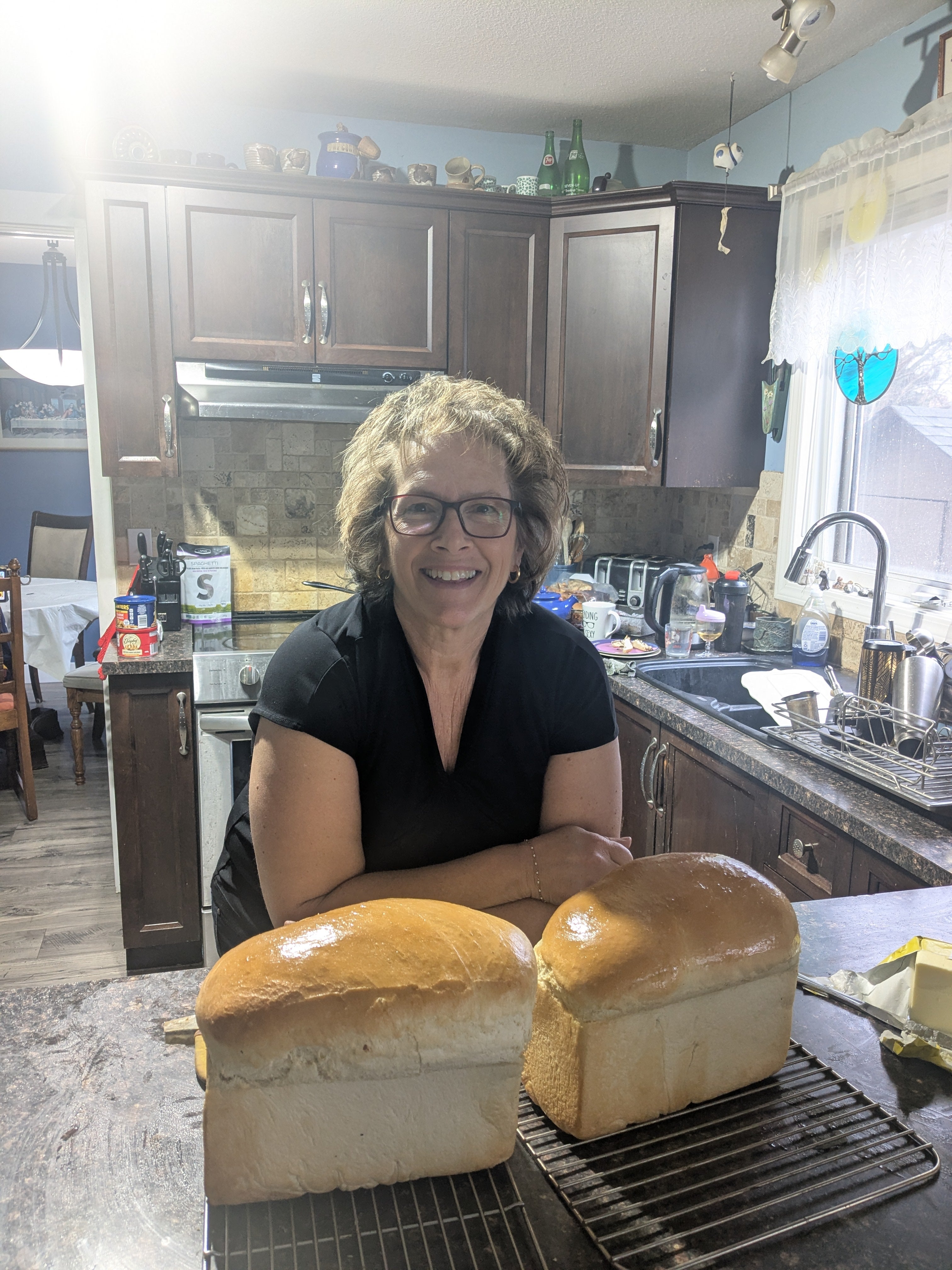 A person leans on a counter, posing with two fresh loaves of baked bread. 