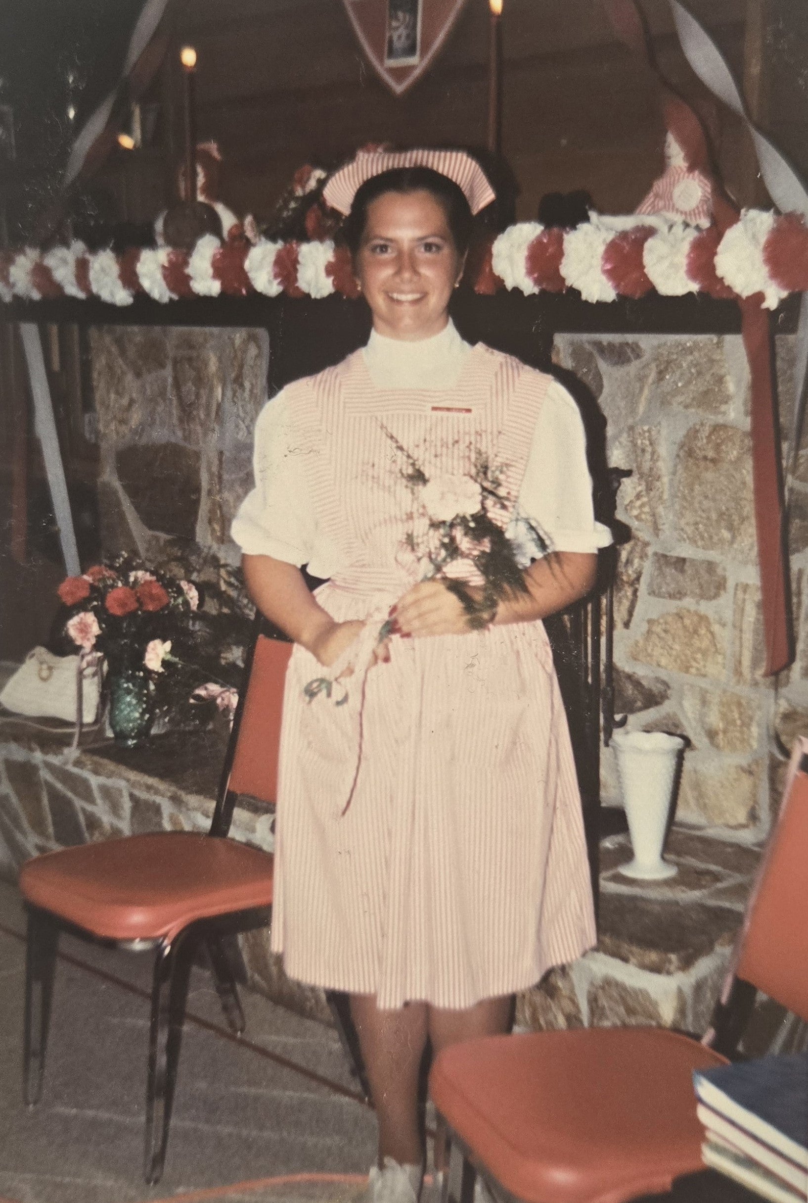 A person wearing a red-and-white-striped uniform stands in front of a stone wall lined with red and white streamers.