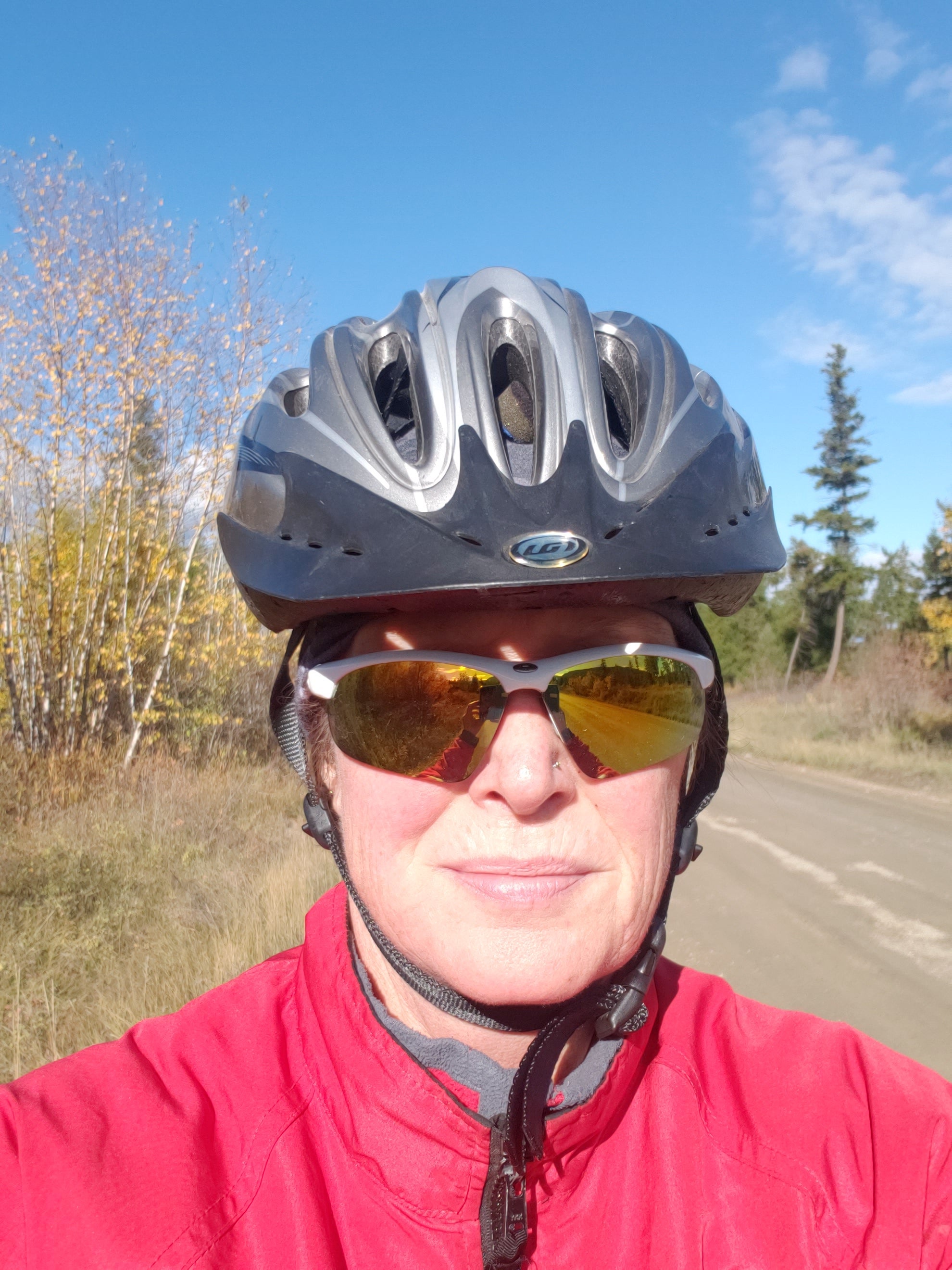 A selfie of a woman wearing a red jacket, sunglasses and a biking helmet.