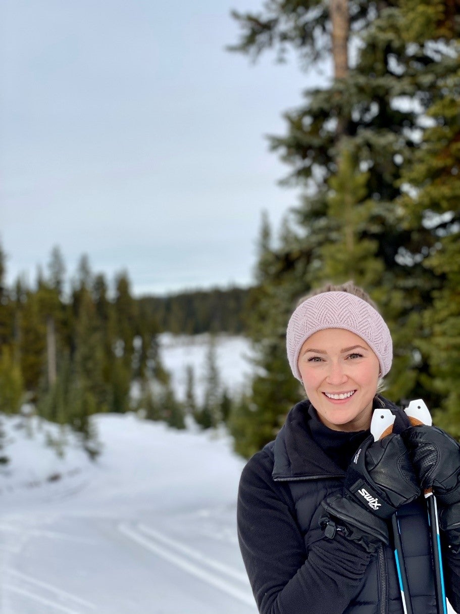 Young woman pauses on a snow trail while resting her hands on her ski poles.