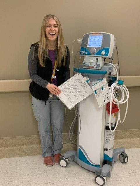 Smiling young woman stands next to a respiratory machine in hospital.