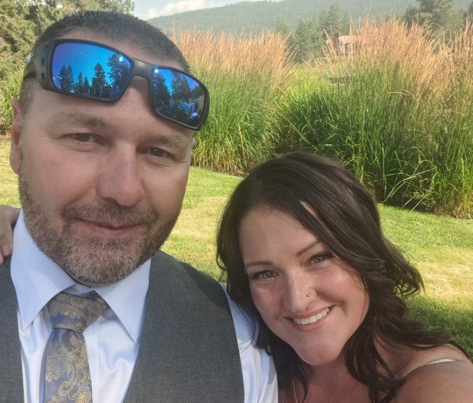 A smiling couple standing close together in a grassy area.