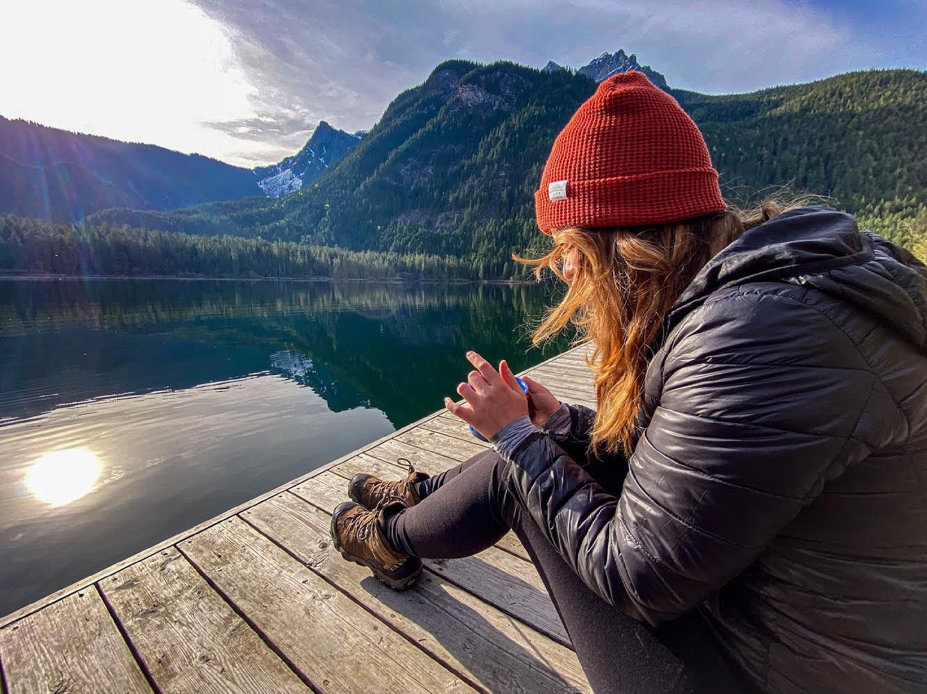 Woman sitting on the dock overlooking a lake and mountains in the distance.